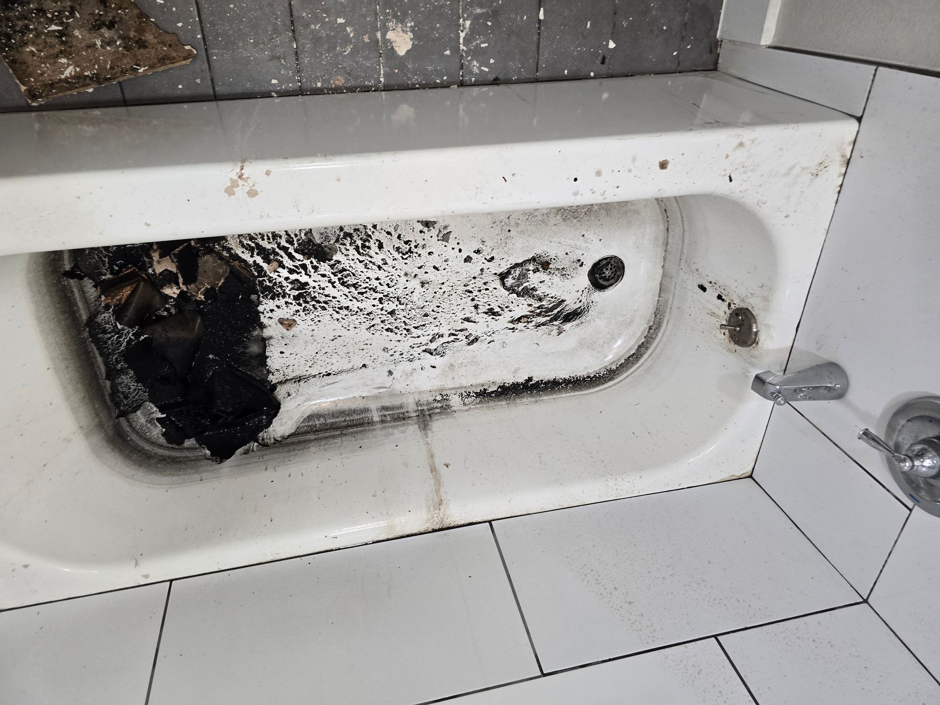 White bathtub with extensive black mold and debris, surrounded by white tile flooring and wall.