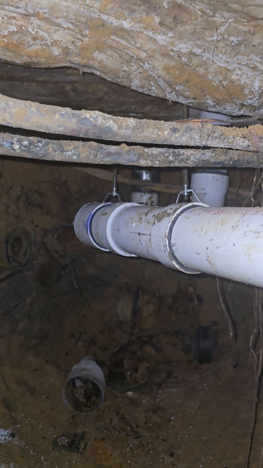 White PVC pipes in a trench, held by metal straps. Dark, enclosed space.