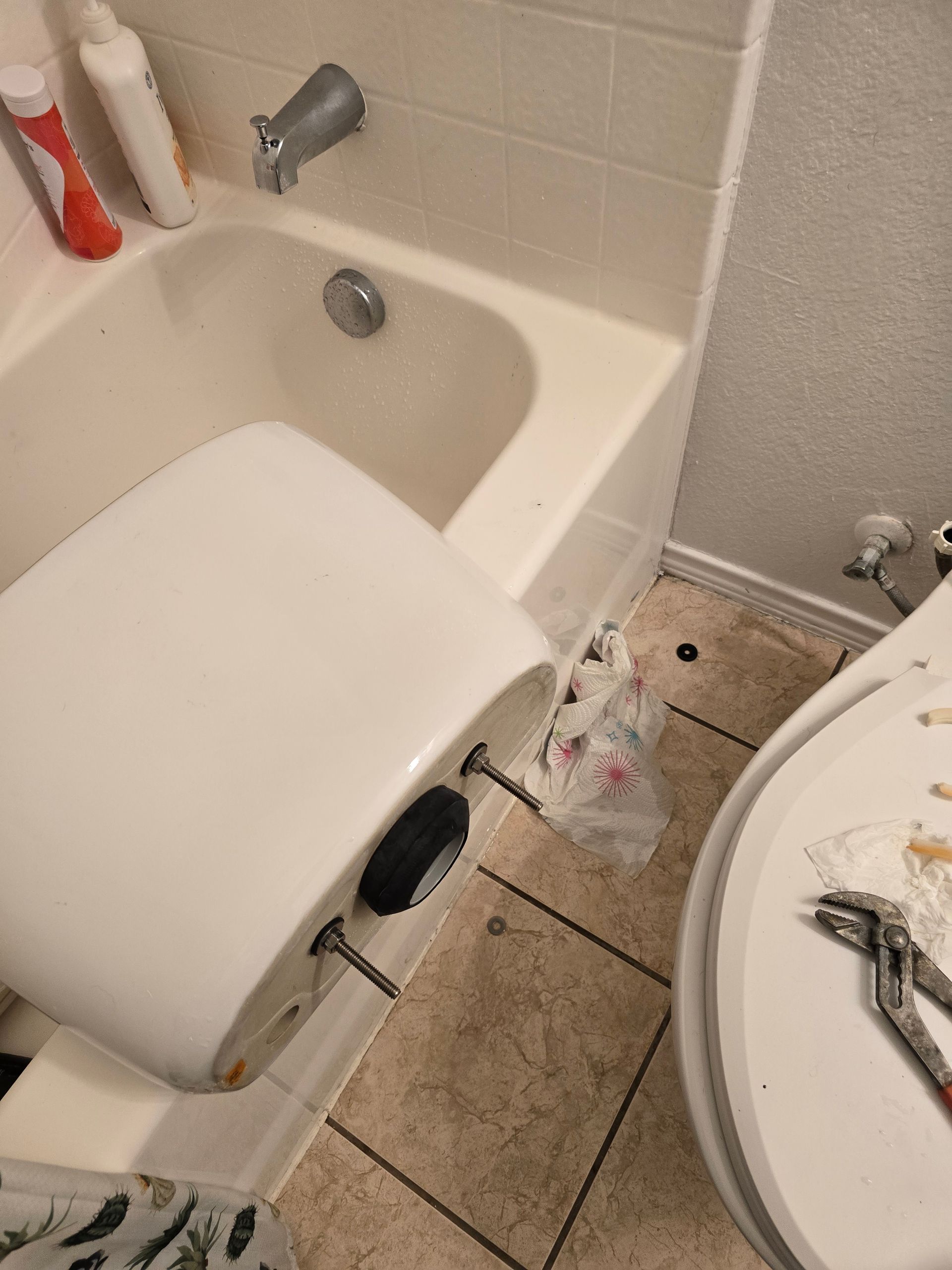 Bathroom with a partially removed toilet next to a bathtub. Plumbing tools and debris are visible.