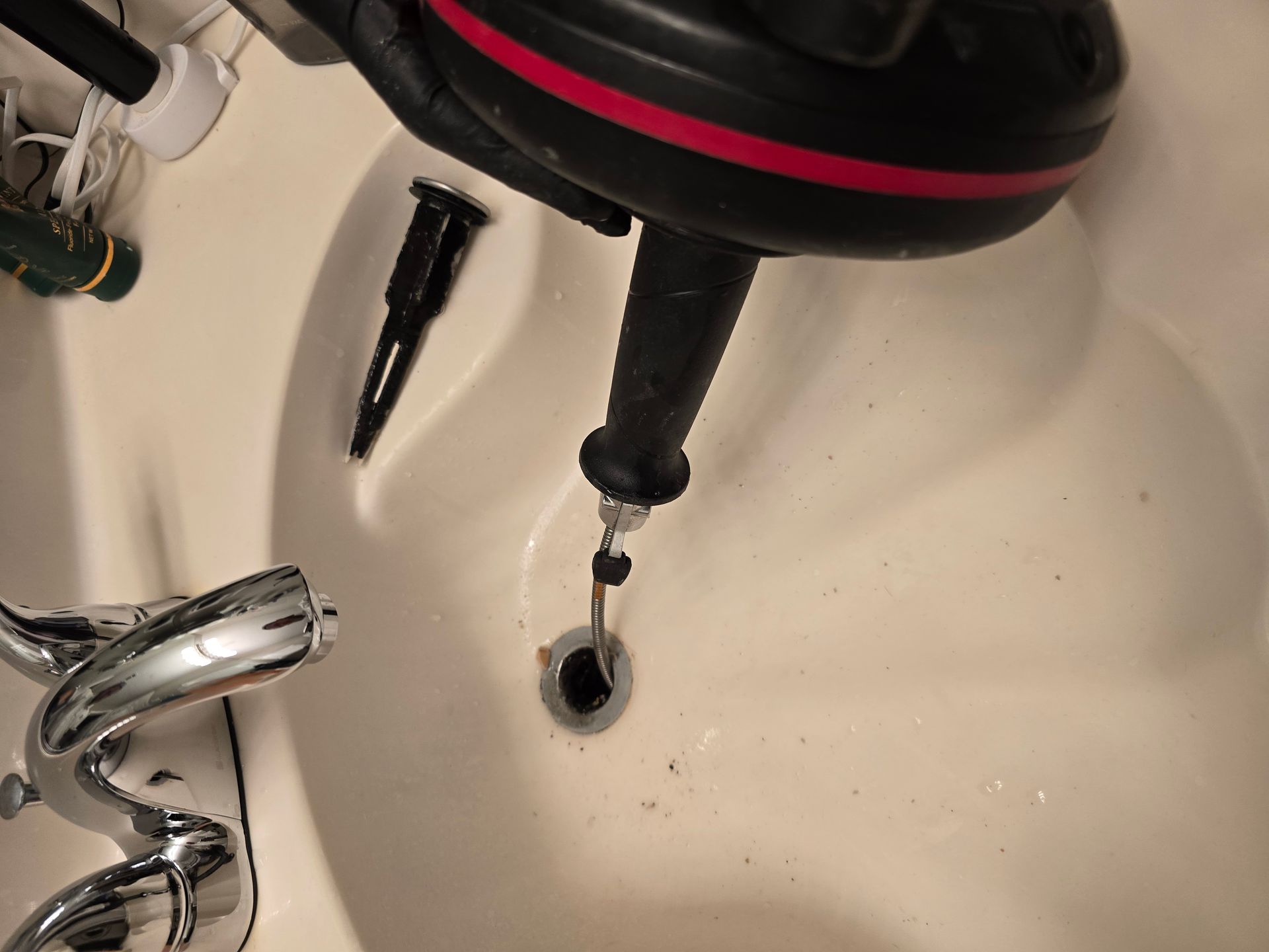 A bathtub drain being unclogged with a black and red plumbing snake.