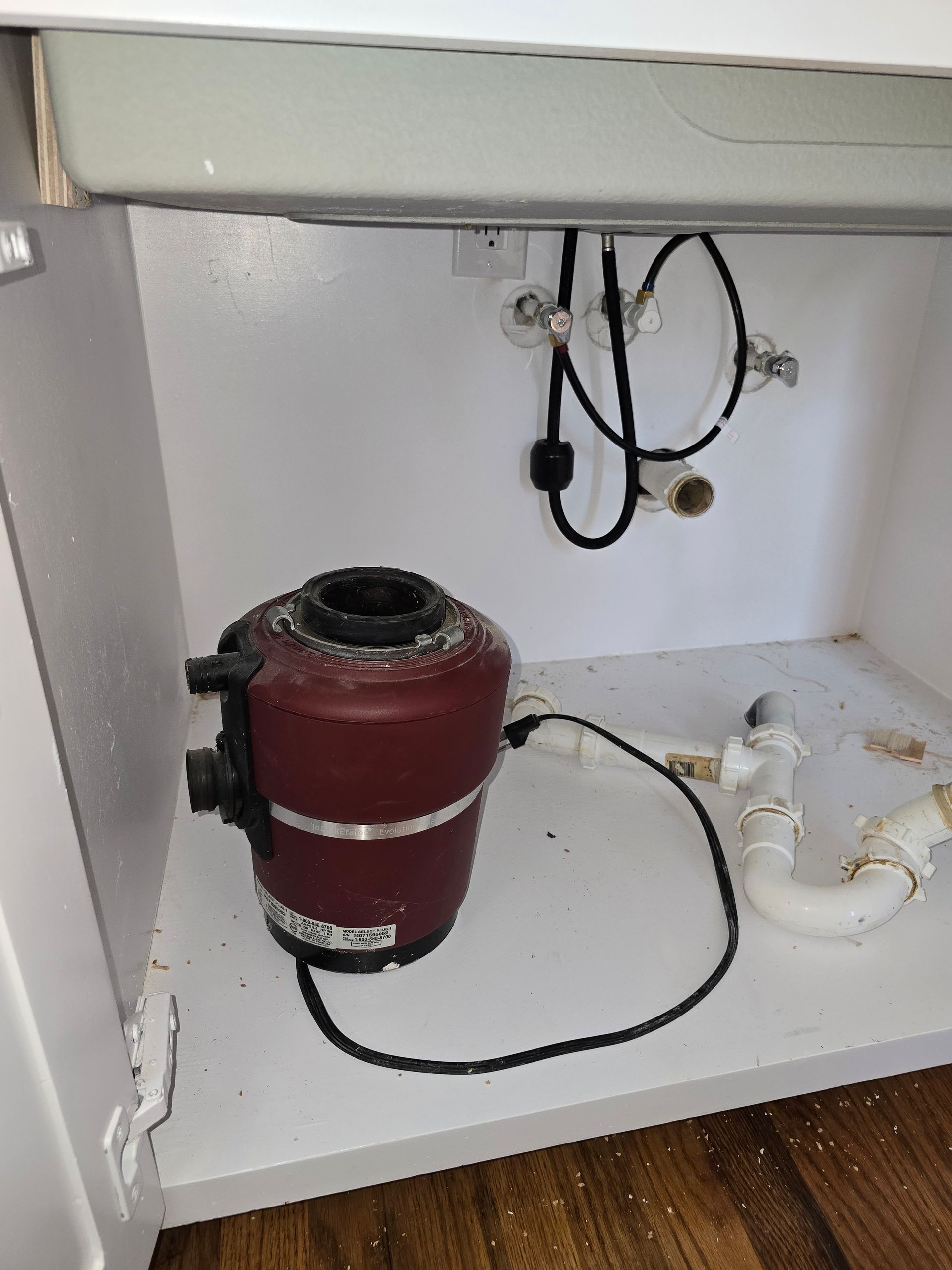 Garbage disposal unit under a white kitchen sink. Plumbing and electrical wiring are visible.