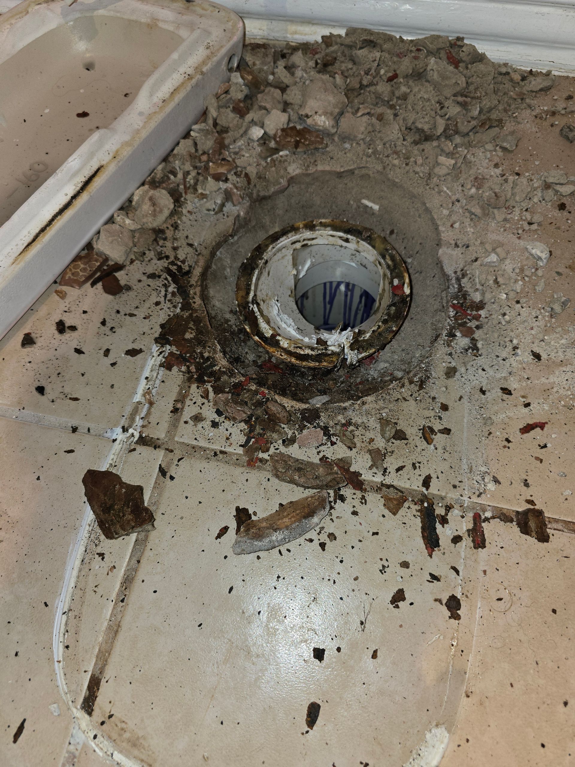 Floor drain with damaged surrounding tiles and debris.