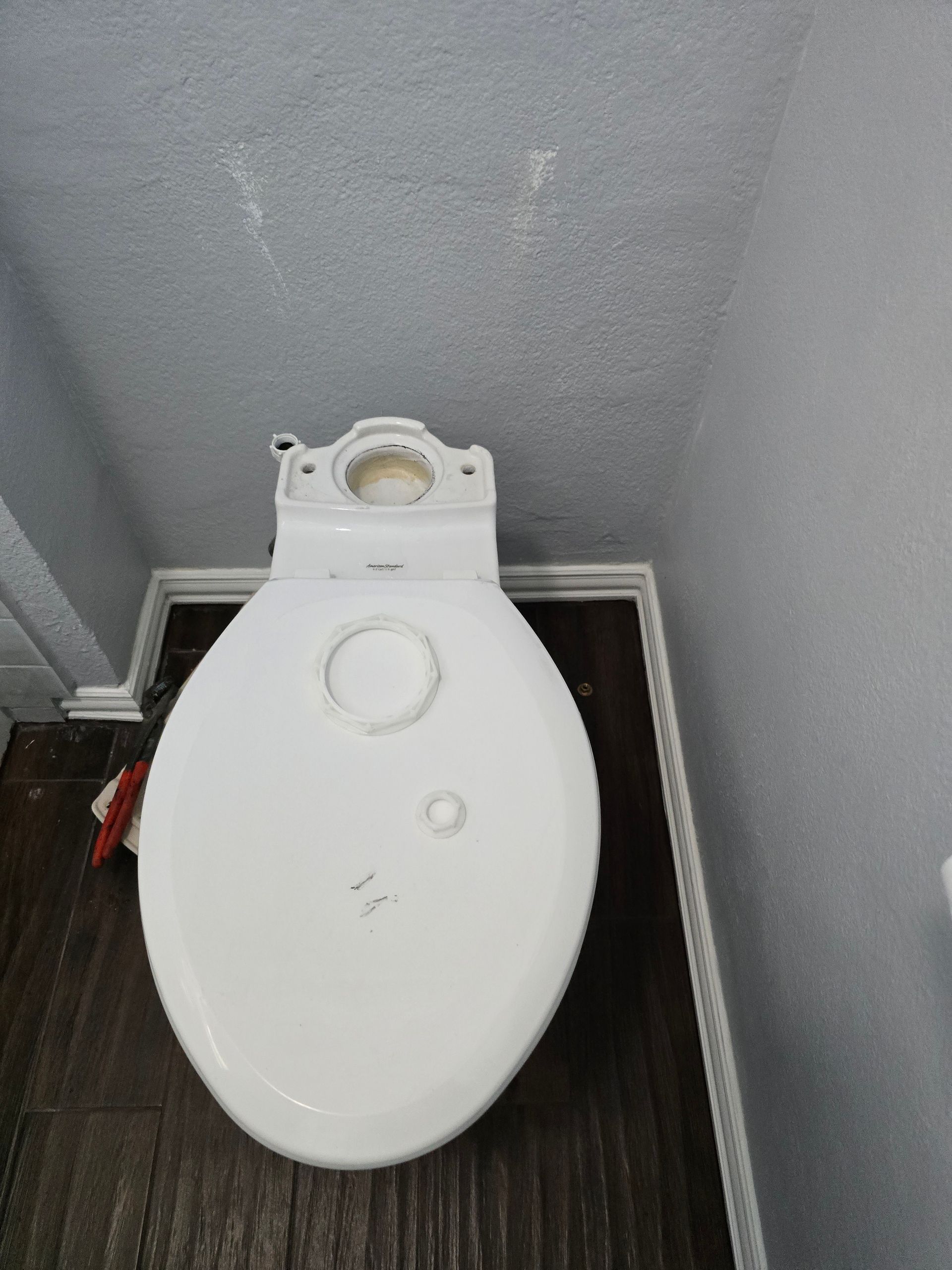 Top-down view of a white toilet bowl. It is surrounded by dark wood-look flooring and gray walls.