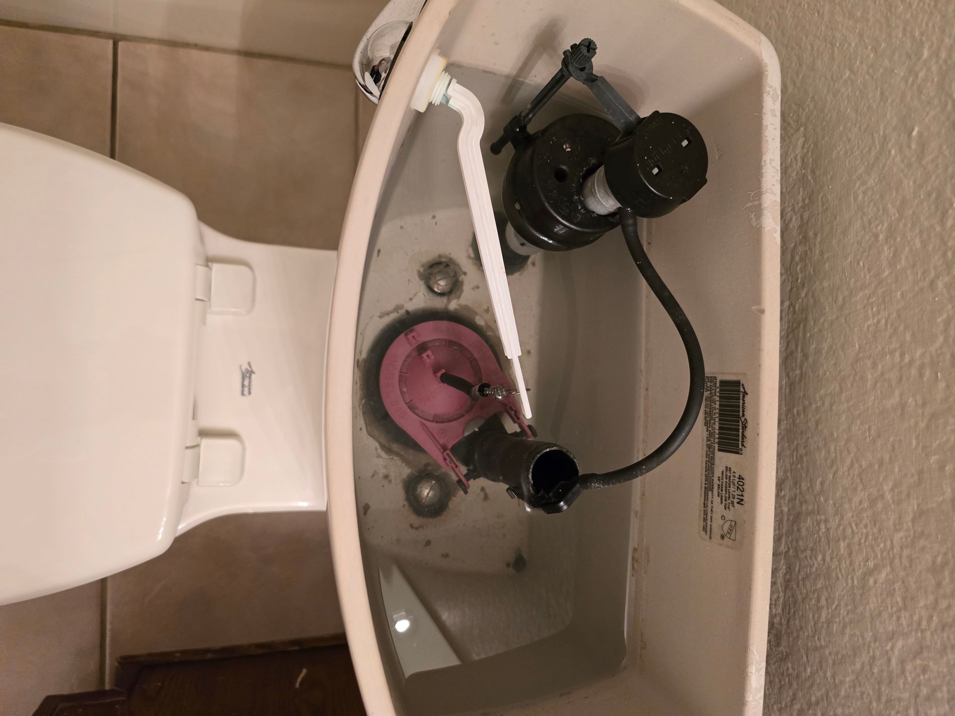 Toilet tank interior with pink flapper, black fill valve, and white arm connected.