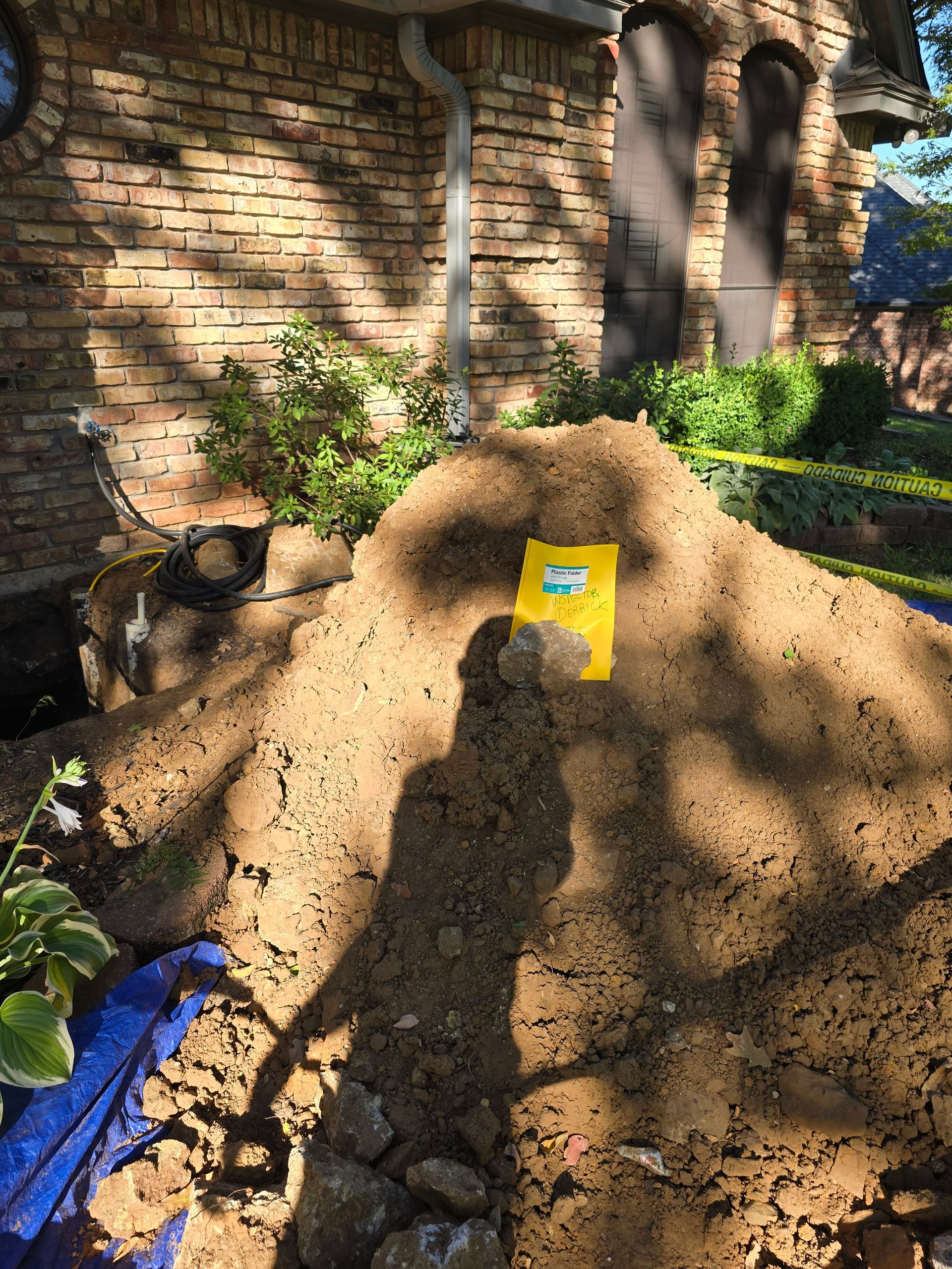 Pile of dirt with a yellow bag, near a brick building with visible shadows.