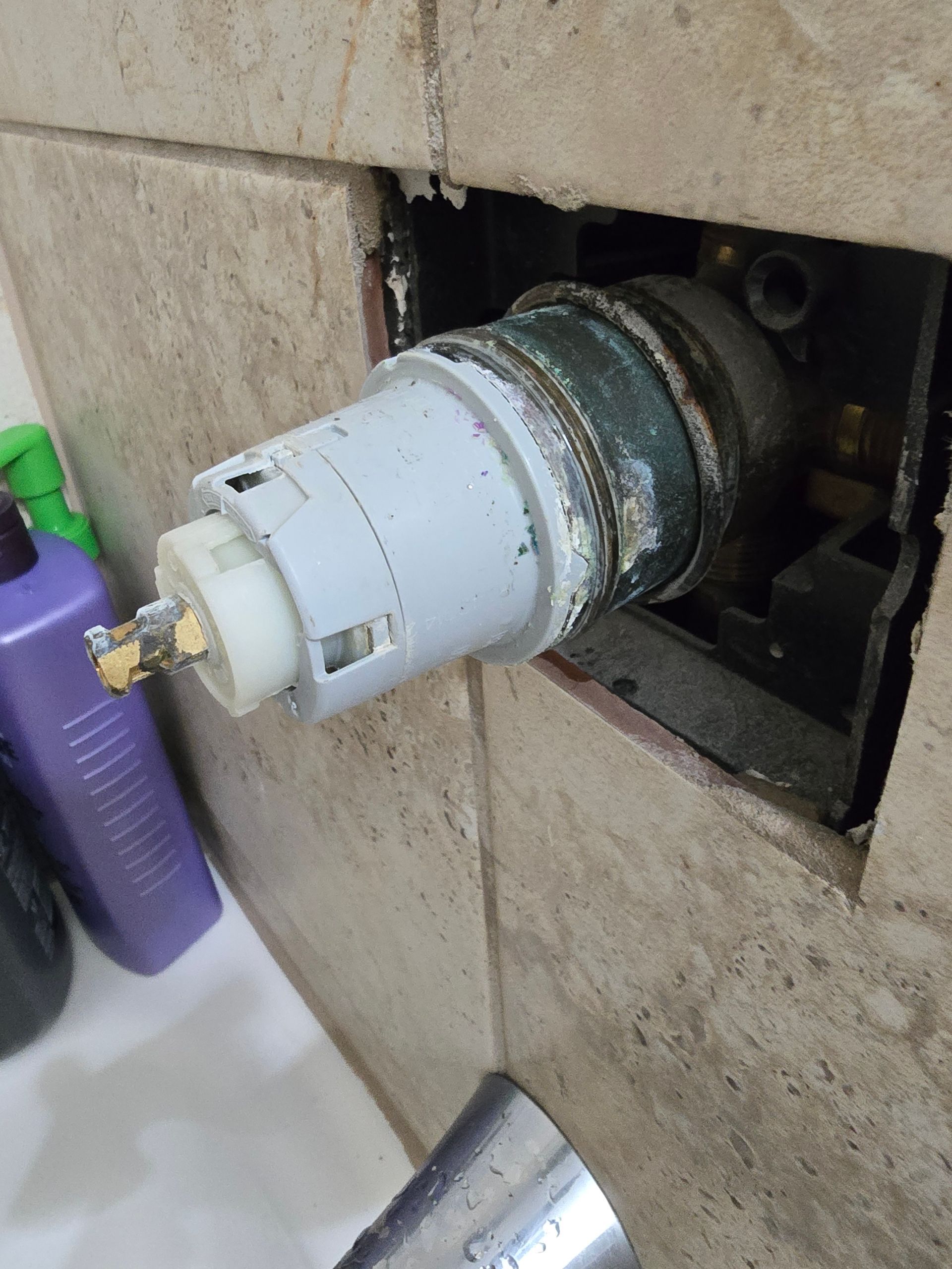 Shower valve cartridge removed from a tile wall. The cartridge is gray and white, surrounded by a metal valve body.