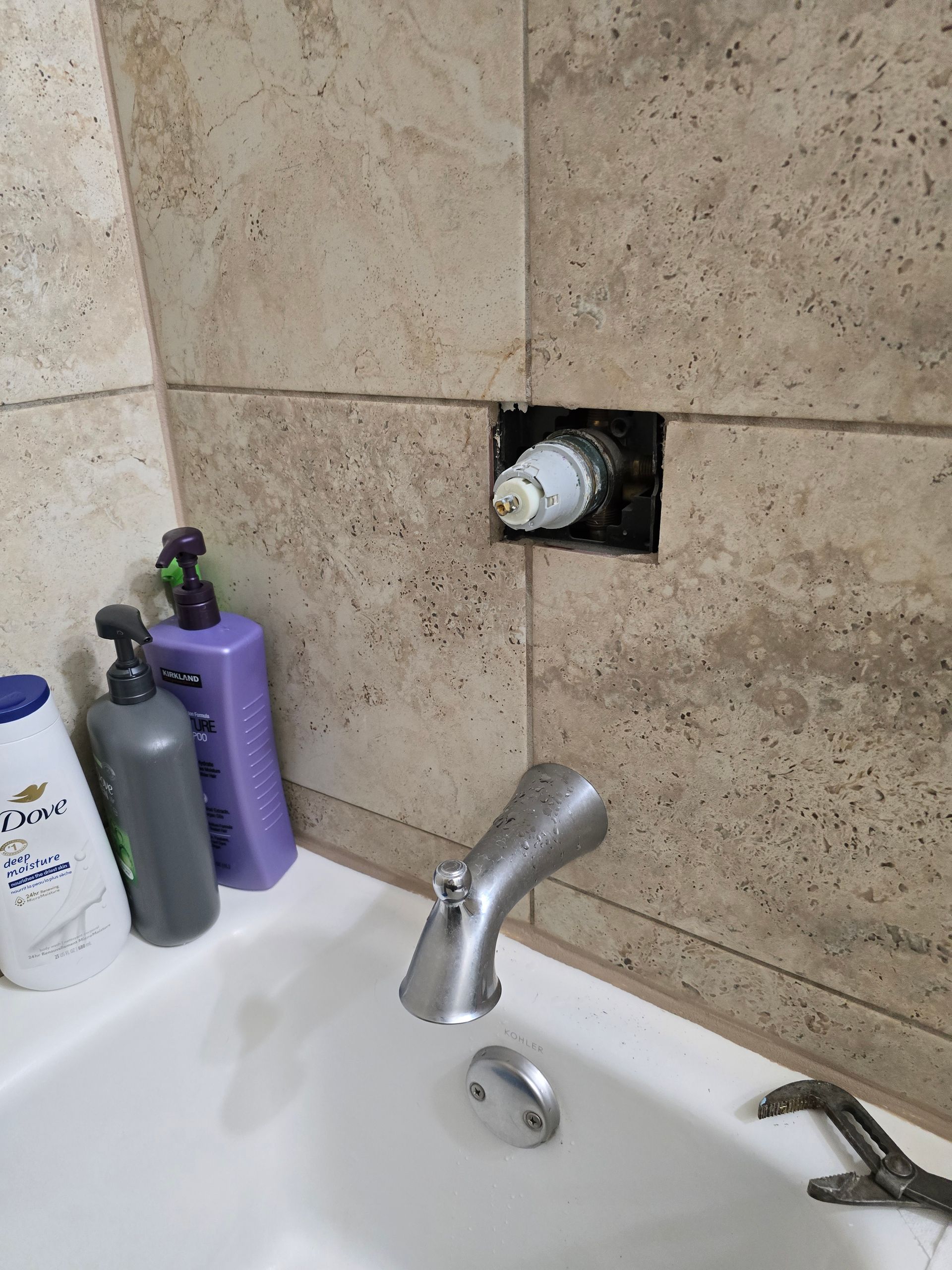 Bathtub with exposed shower valve in a tiled wall; a wrench sits on the tub rim.