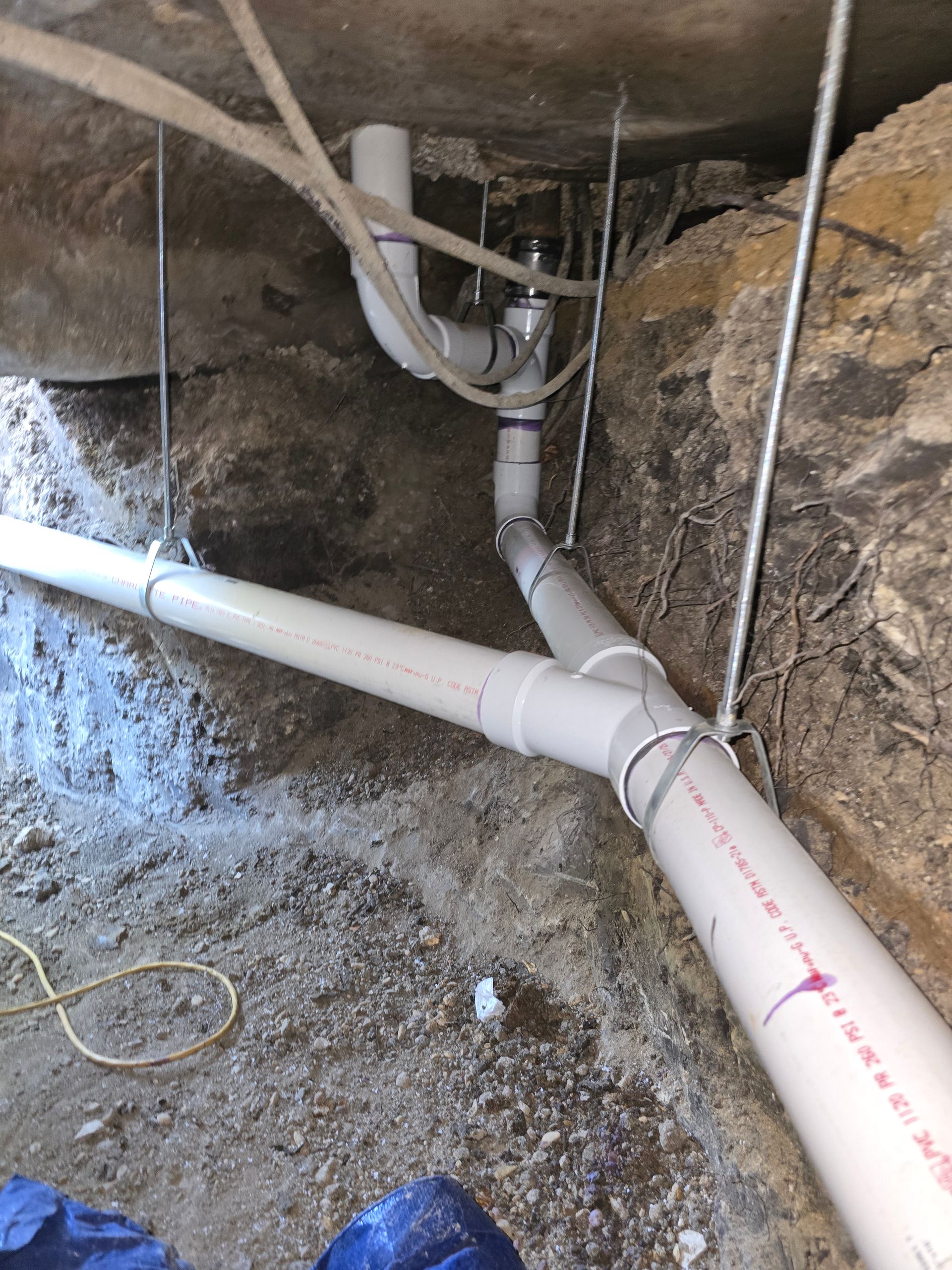 White PVC pipes and fittings within a rocky, underground space, likely plumbing installation.