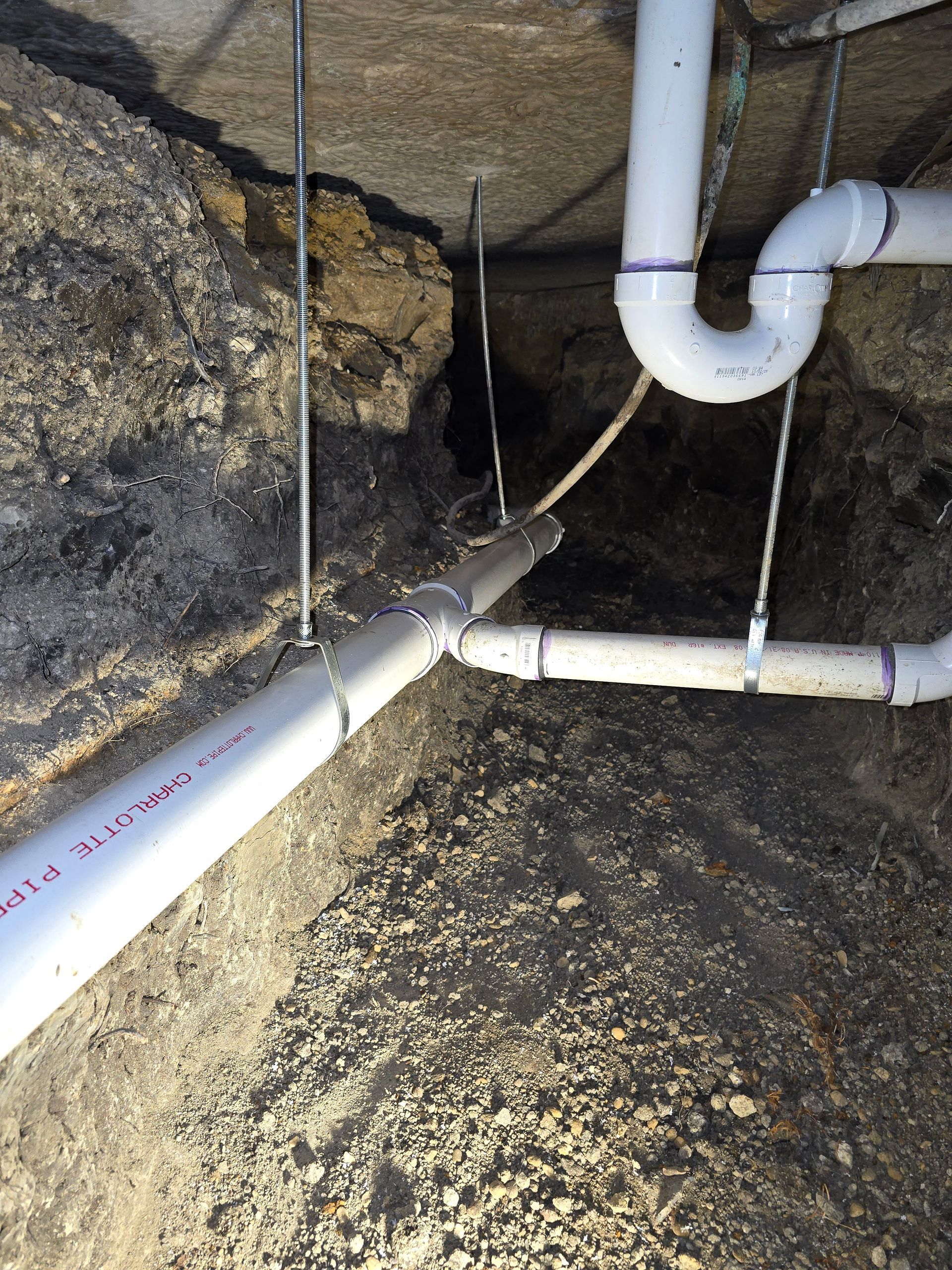 White PVC plumbing pipes against a dirt and rock wall, with metal supports.