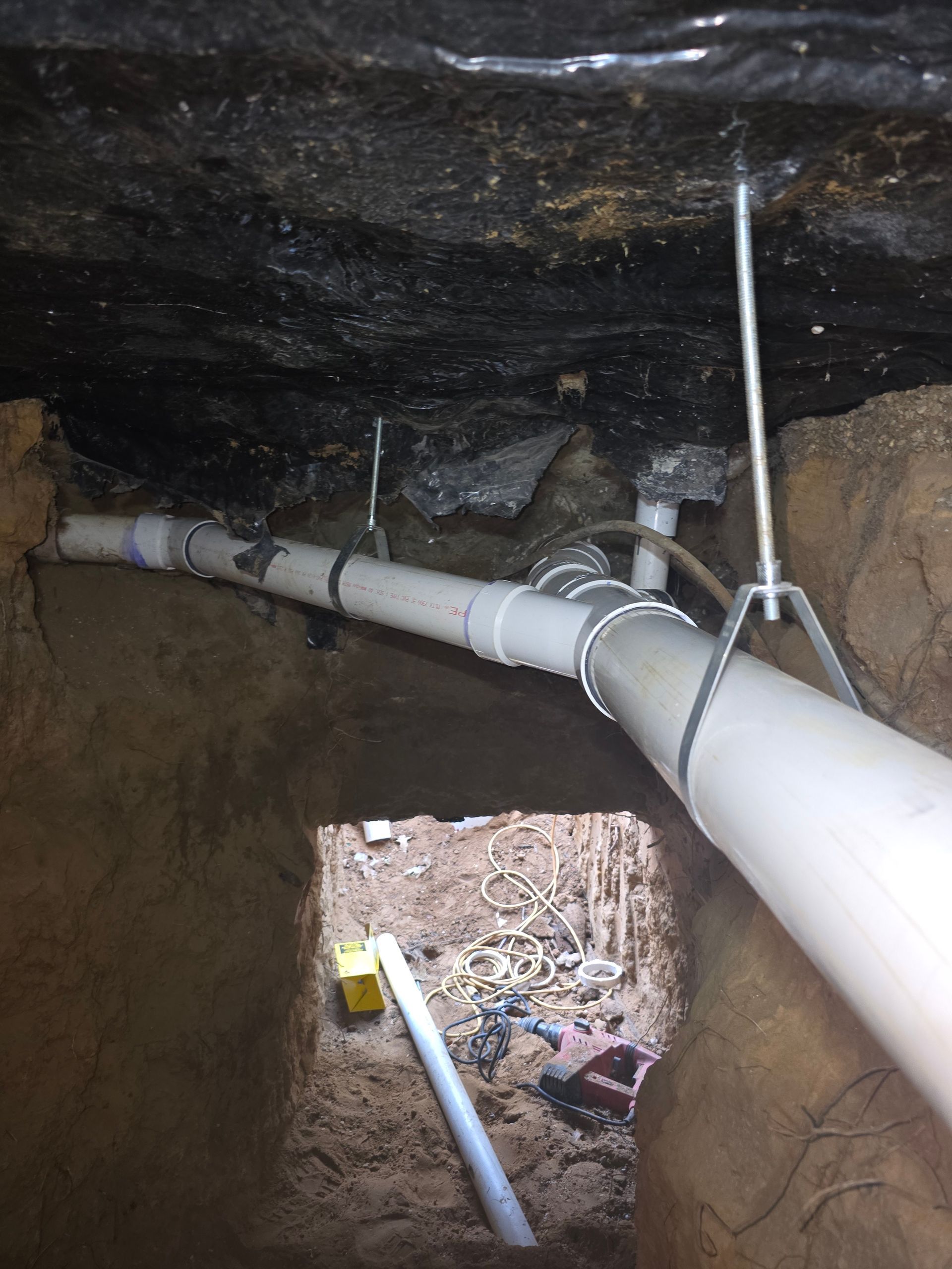 White PVC pipes installed in a narrow underground trench. Pipes are supported by metal hangers.