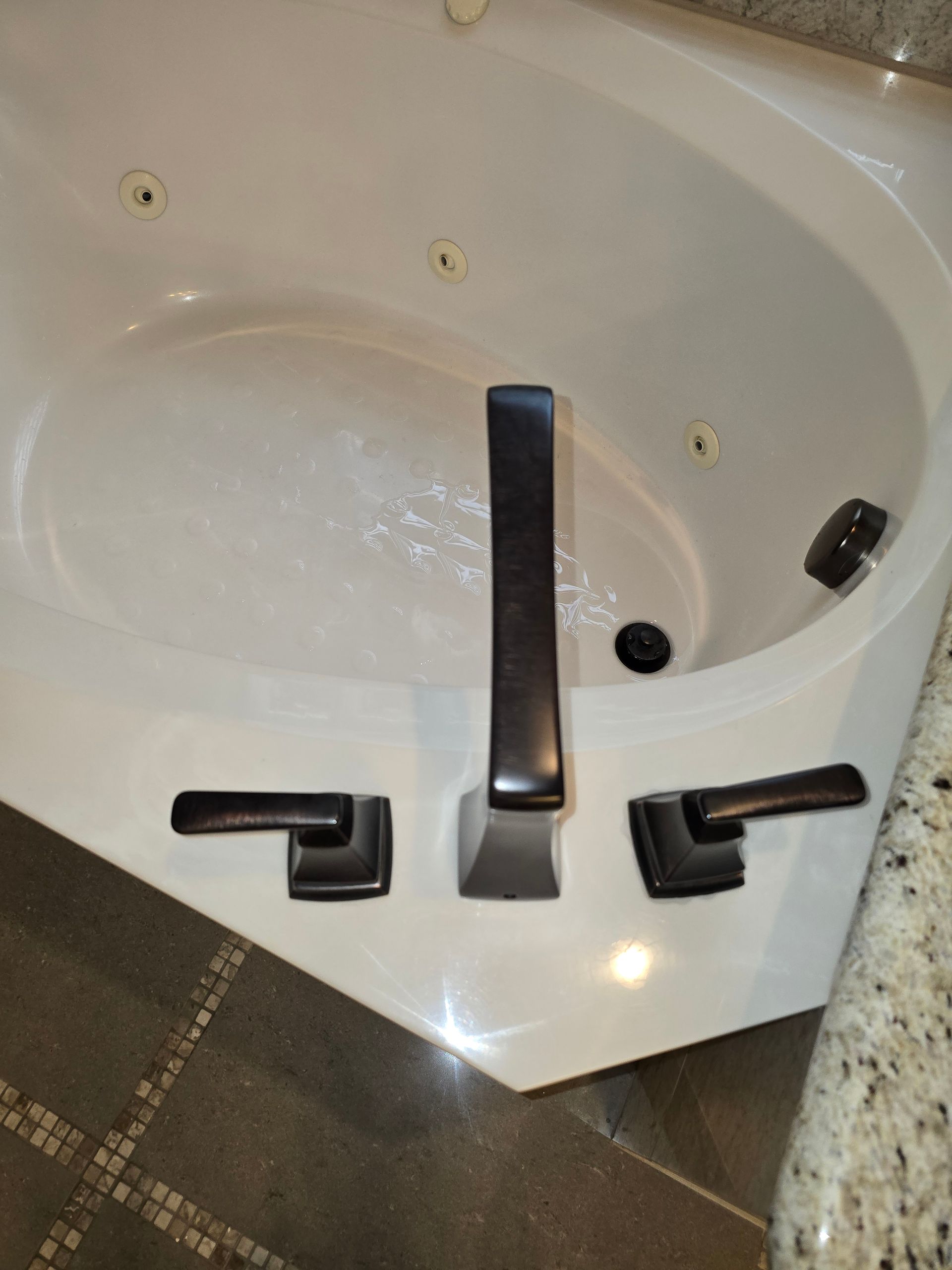 Corner jacuzzi tub with dark bronze faucet and handles.