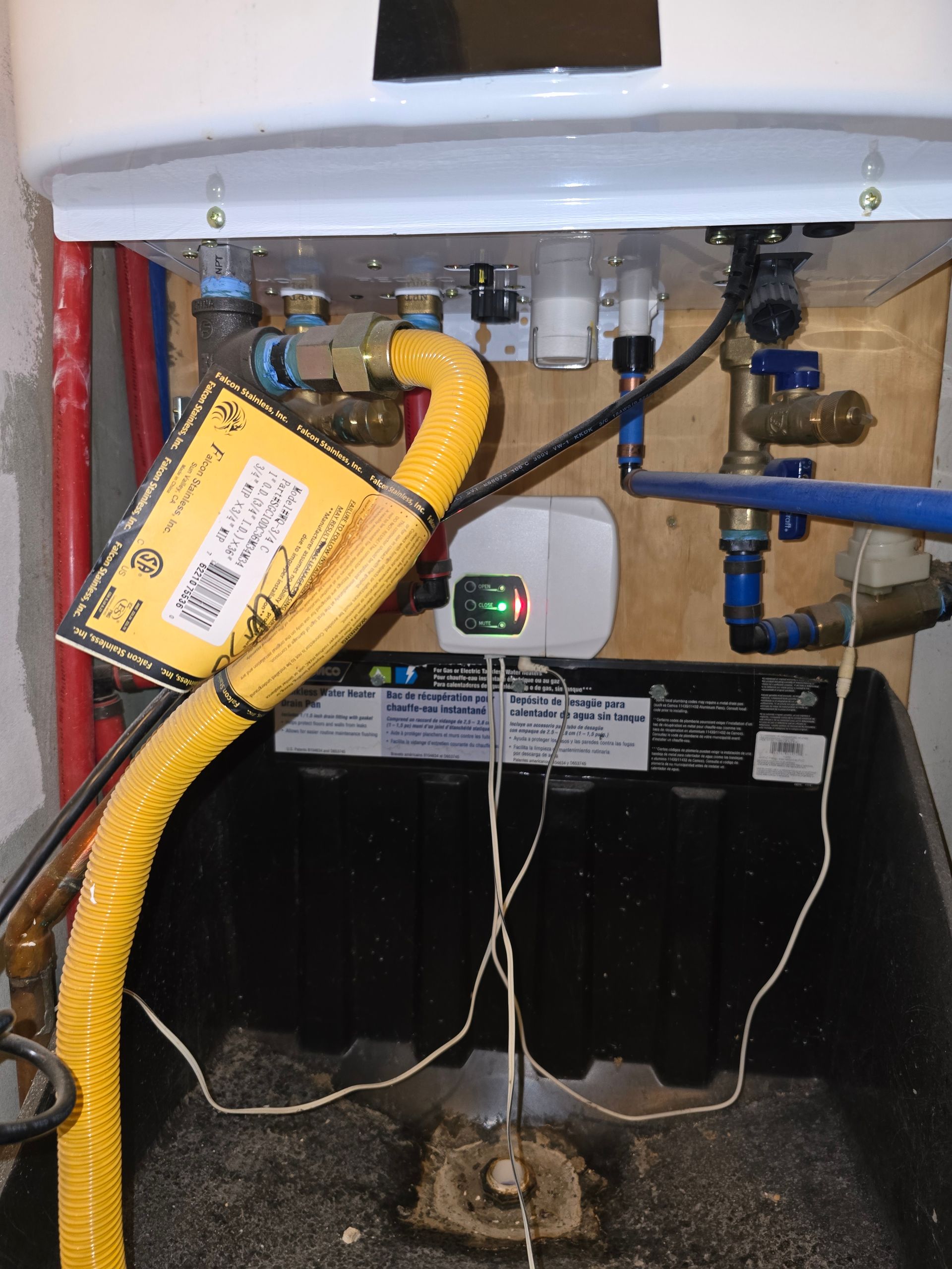 A tankless water heater with yellow exhaust pipe, various pipes, and wires.