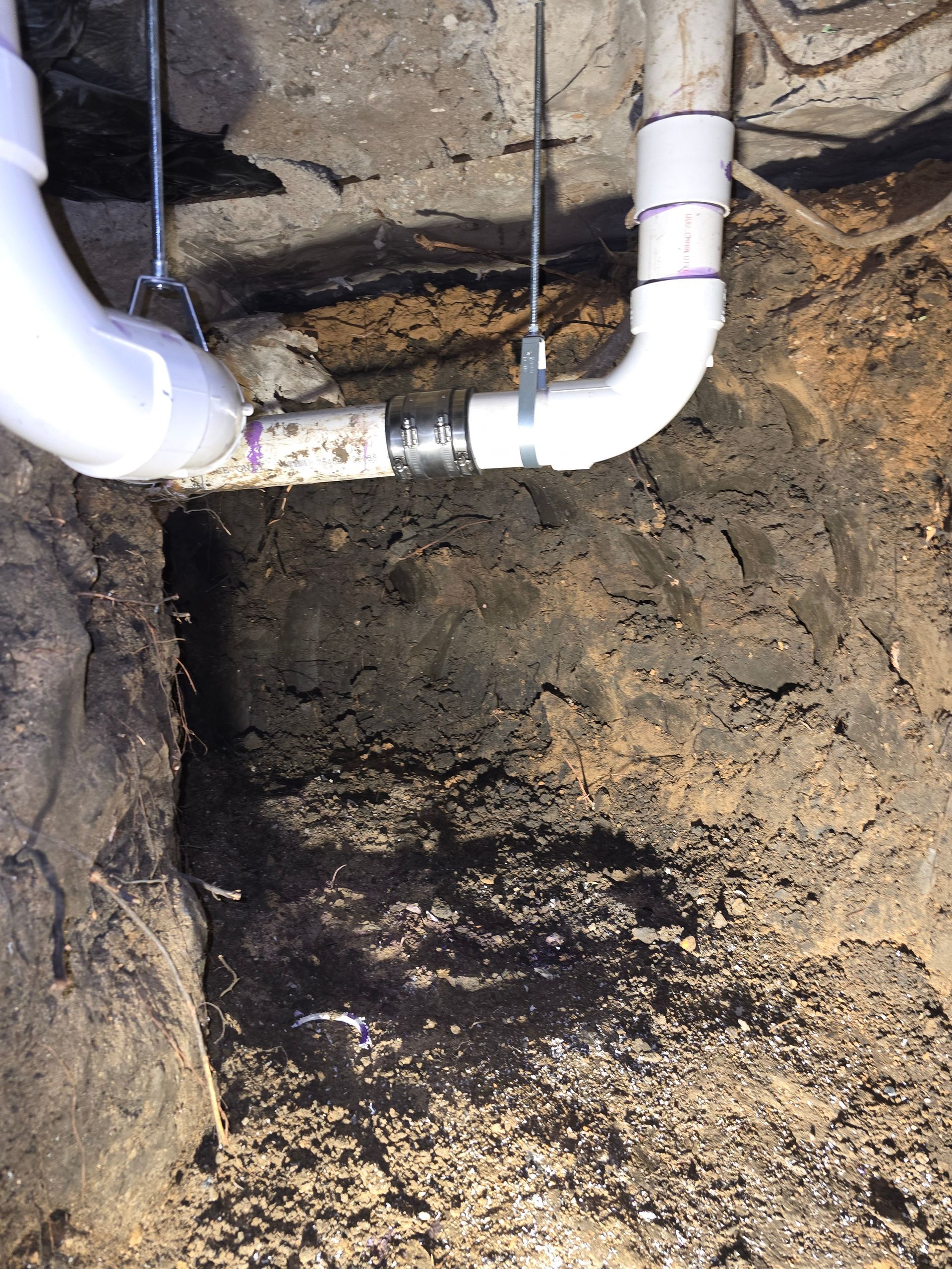 White PVC pipes and fittings in a dirt trench, connected with a metal coupling.