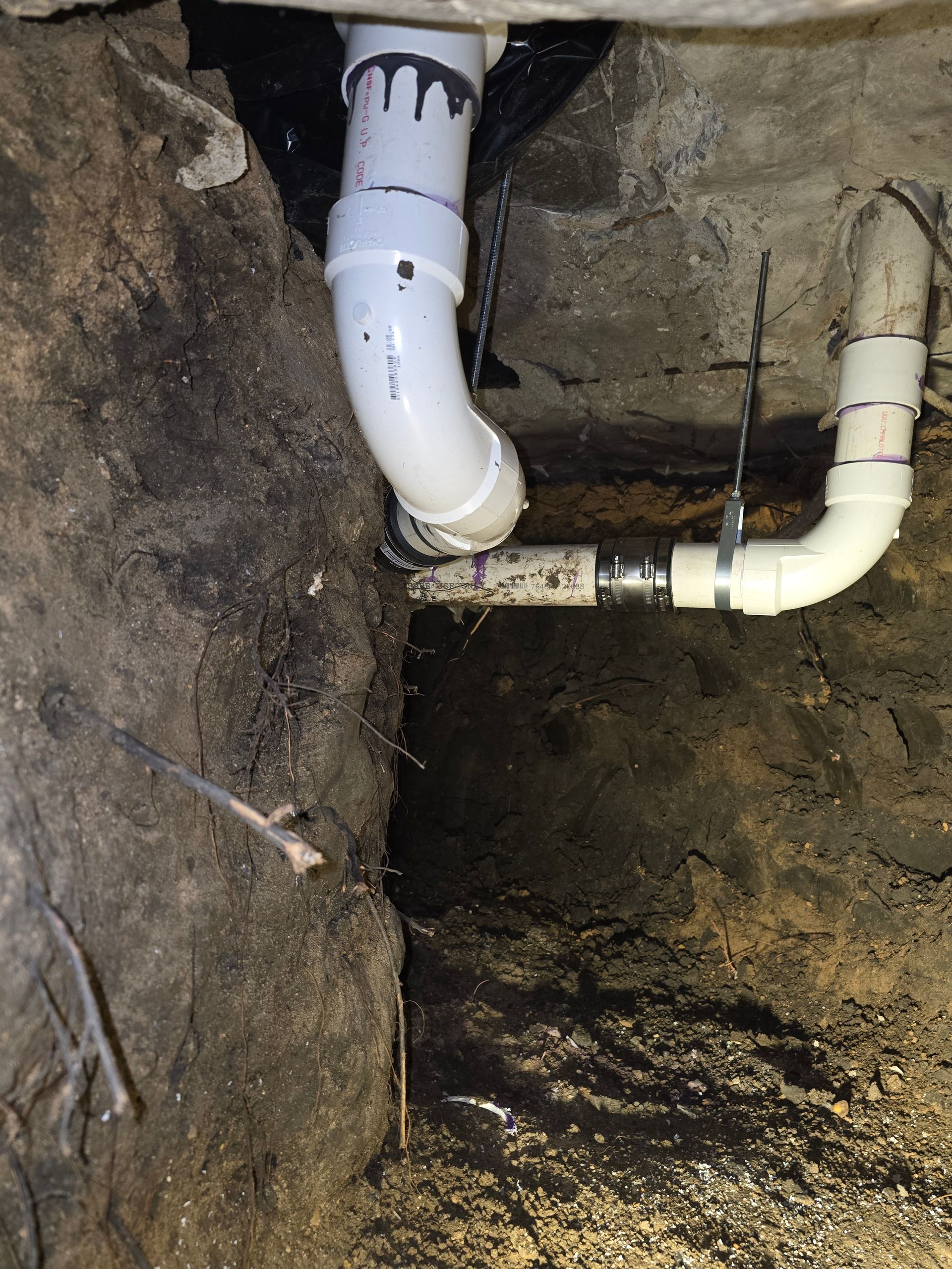 White PVC plumbing pipes against a dark, rough stone foundation.