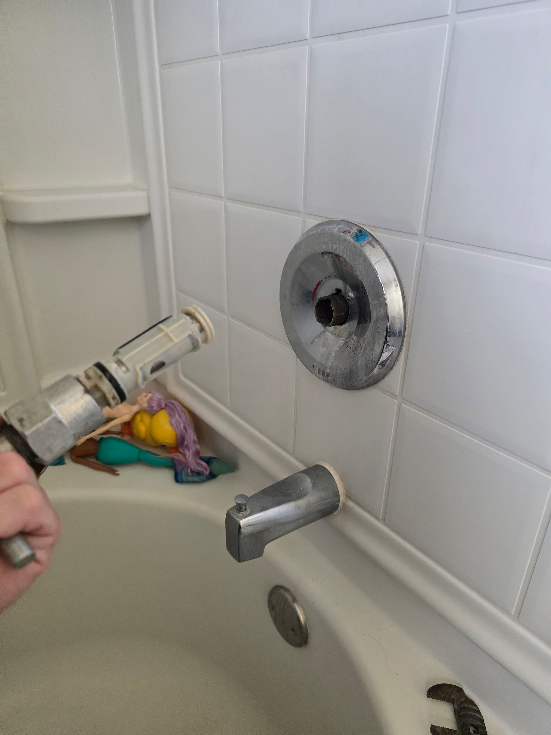Plumber in bathroom, kneeling with plumbing parts, surrounded by tools near toilet.