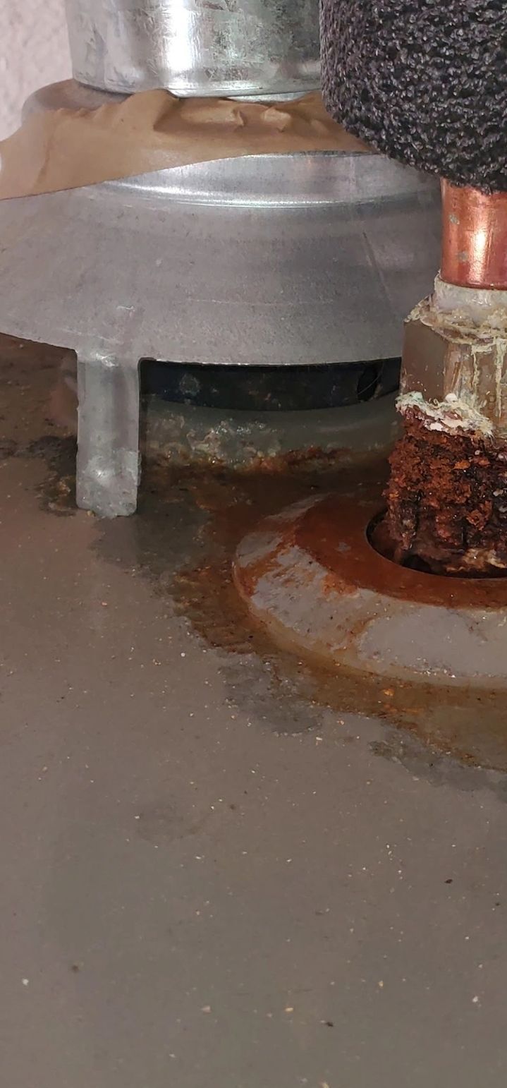 A rusty water heater tank with water damage, possibly leaking around fittings.