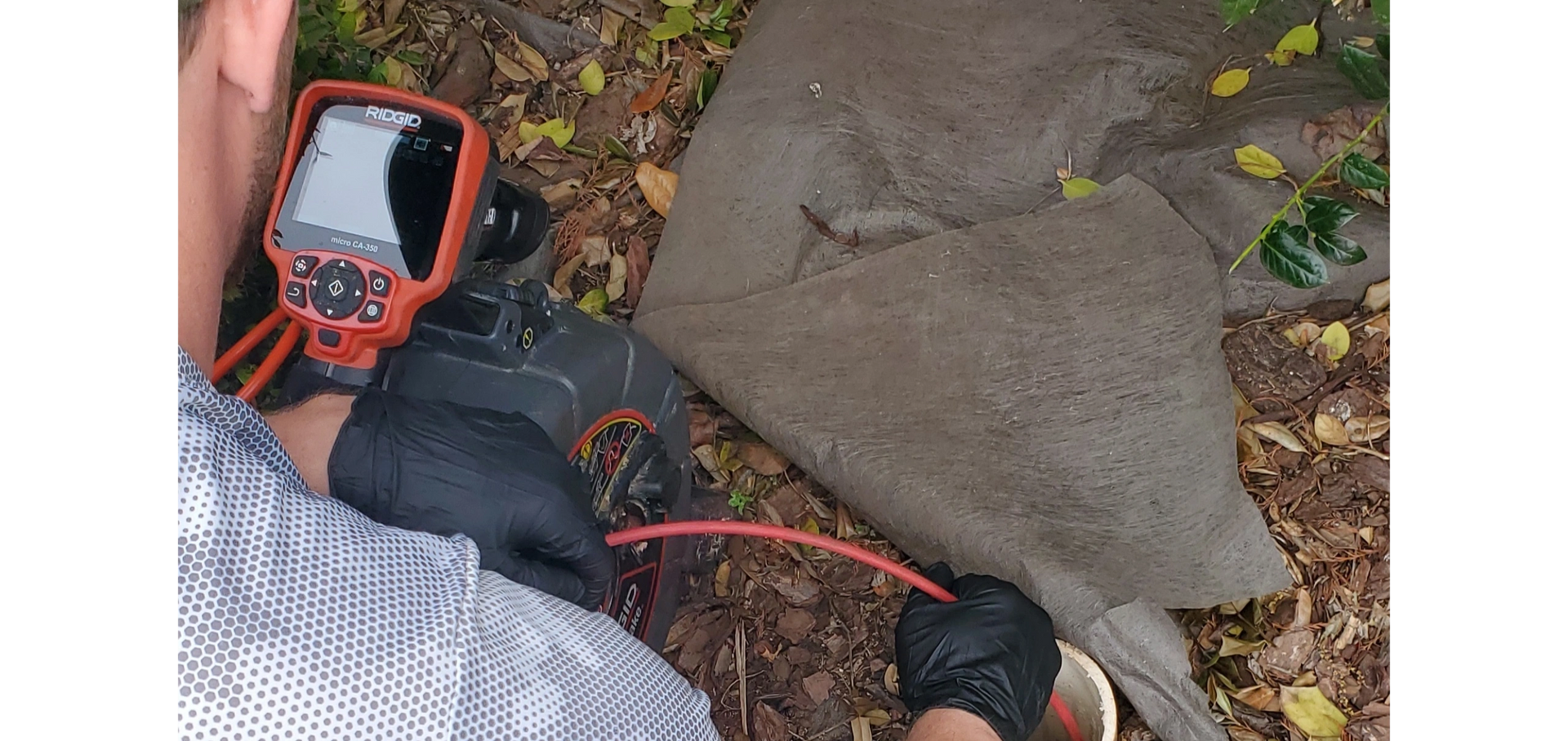 A person inspects with a camera on a screen. The person wears black gloves, and is next to an old, large piece of cloth.