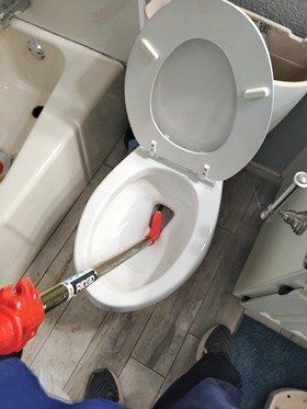 A person using a toilet auger to unclog a toilet. Bathroom setting.