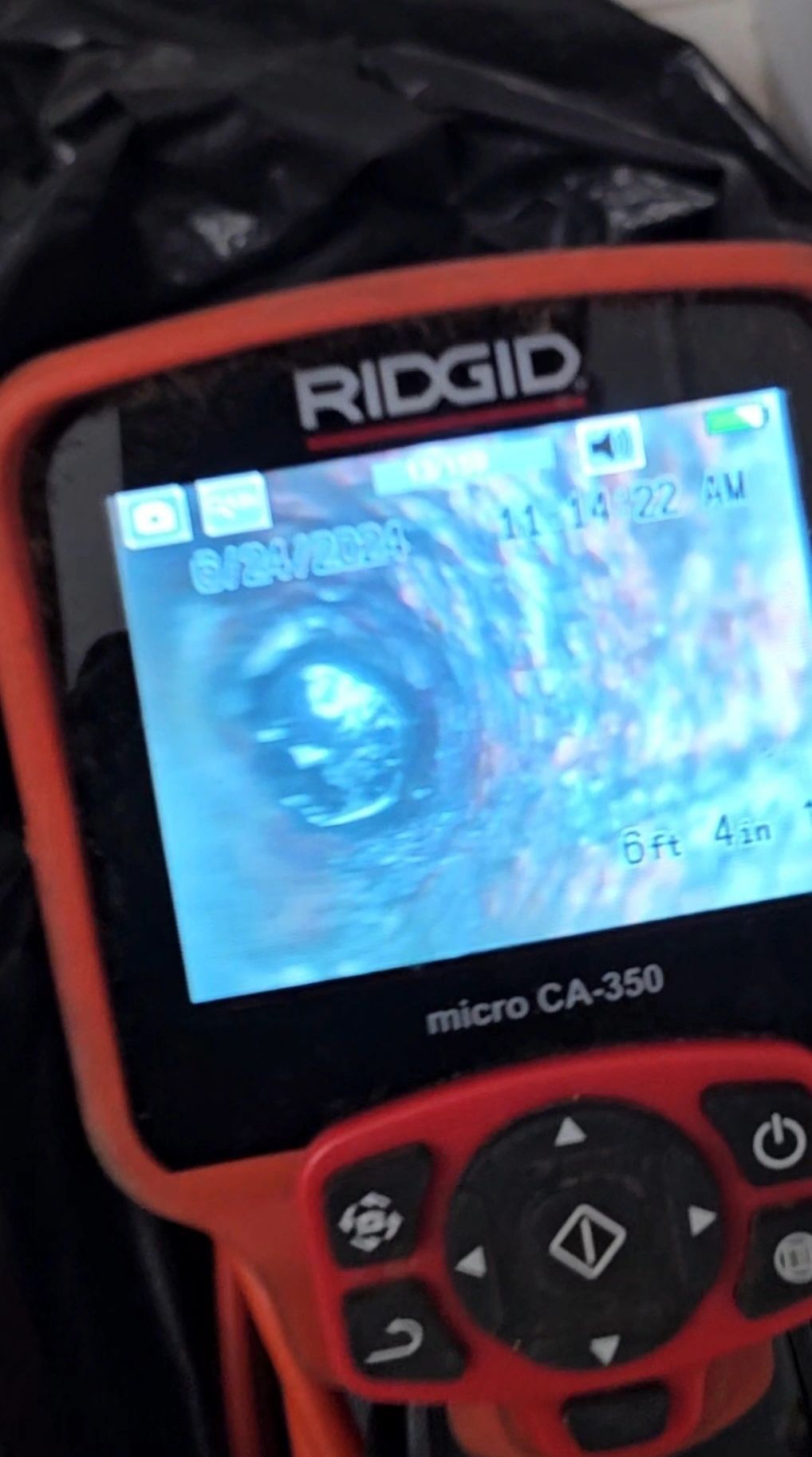 RIDGID micro CA-350 inspection camera displaying a blurry view inside a pipe. Orange and black device.
