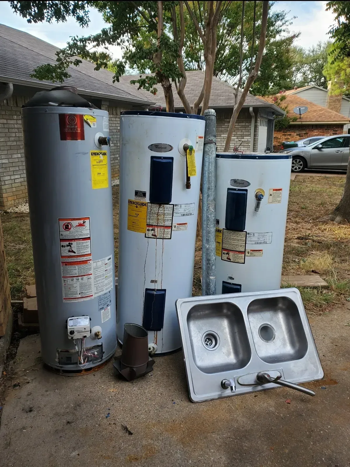 Three water heaters and a double sink sit outside a home.