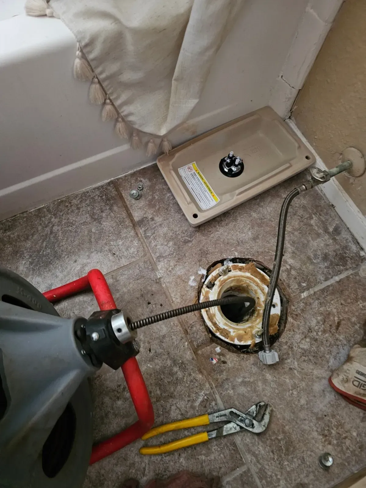 Plumber unclogging a toilet with a snake tool in a bathroom. Toilet base, tools, and equipment on the floor.
