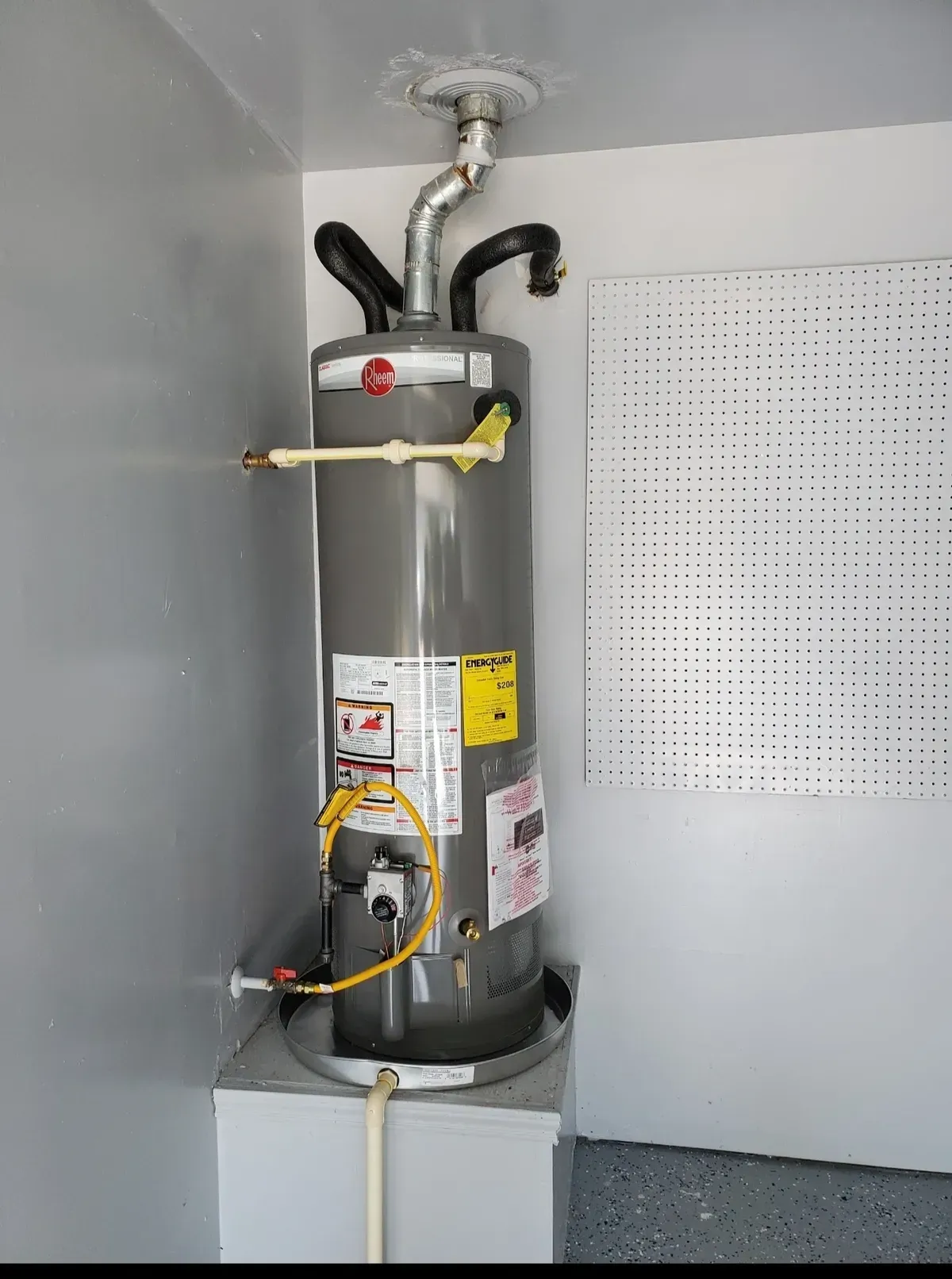 Gray water heater in a garage, with pipes and electrical components.