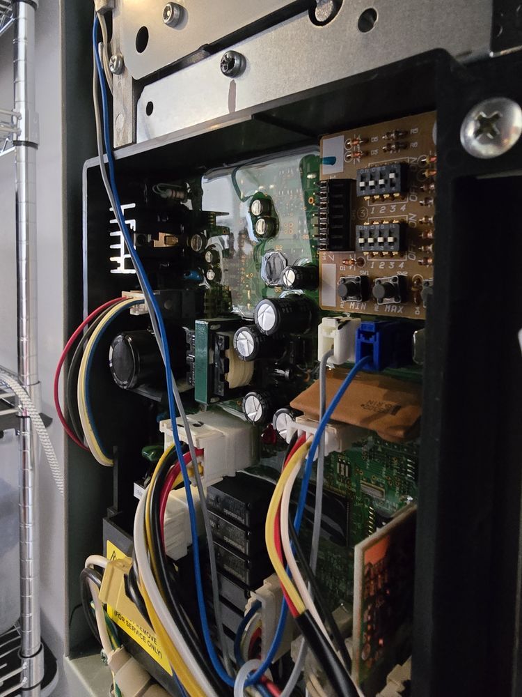 Open electrical panel with circuit boards, wires, and a small fan.