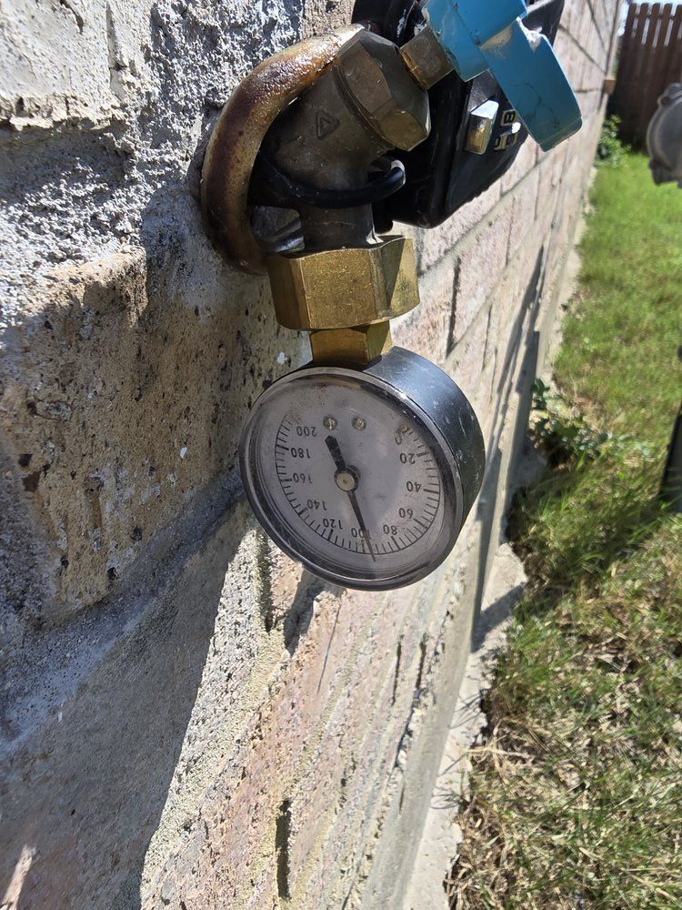 Pressure gauge attached to a water spigot on a brick wall, needle at 50 PSI.