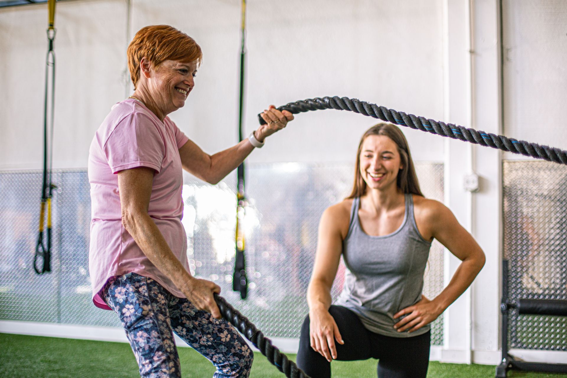 Woman spotter assisting another woman doing dumbbell chest press on a bench in gym.