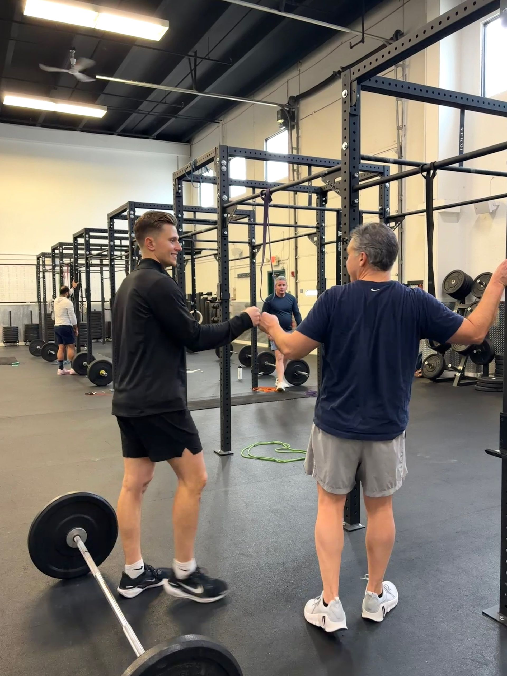 Trainer guides a man holding a kettlebell in a gym, adjusting his grip.