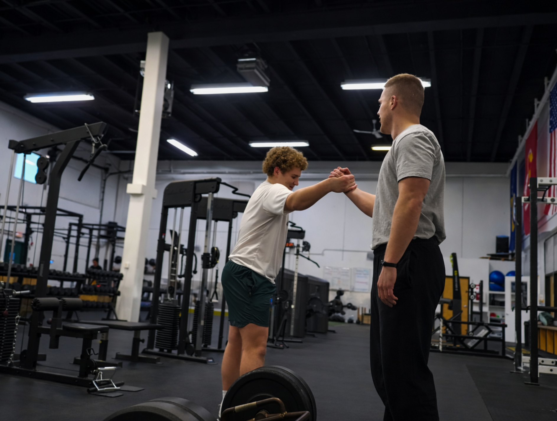 Group of young men in a gym, listening to someone in red shorts.