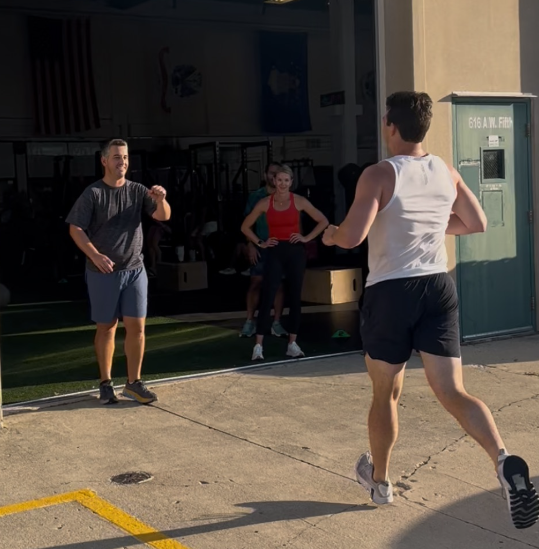 Group of young men in a gym, listening to someone in red shorts.
