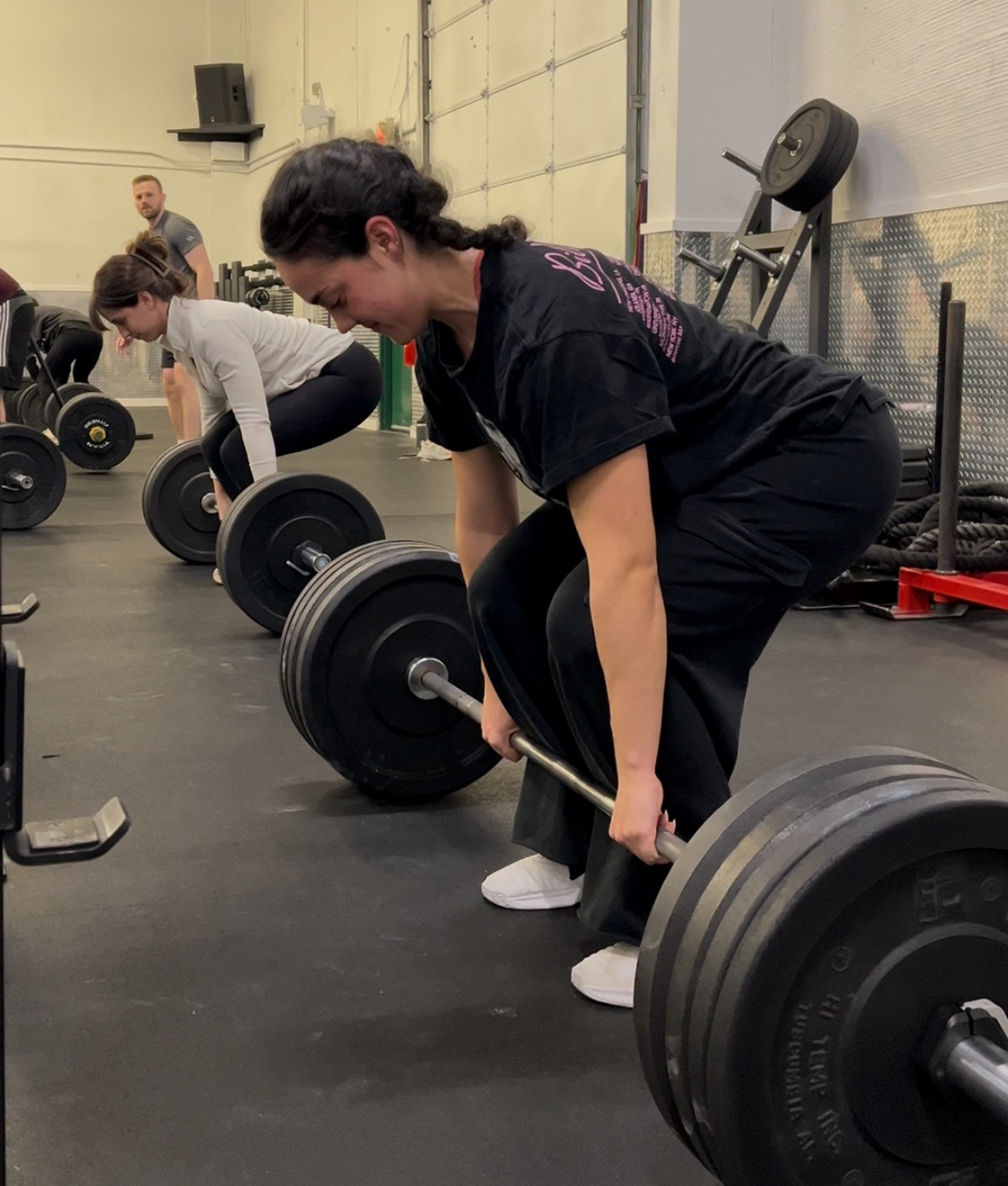 Woman rowing indoors on Concept2 machine. Another person in background. Gym setting.