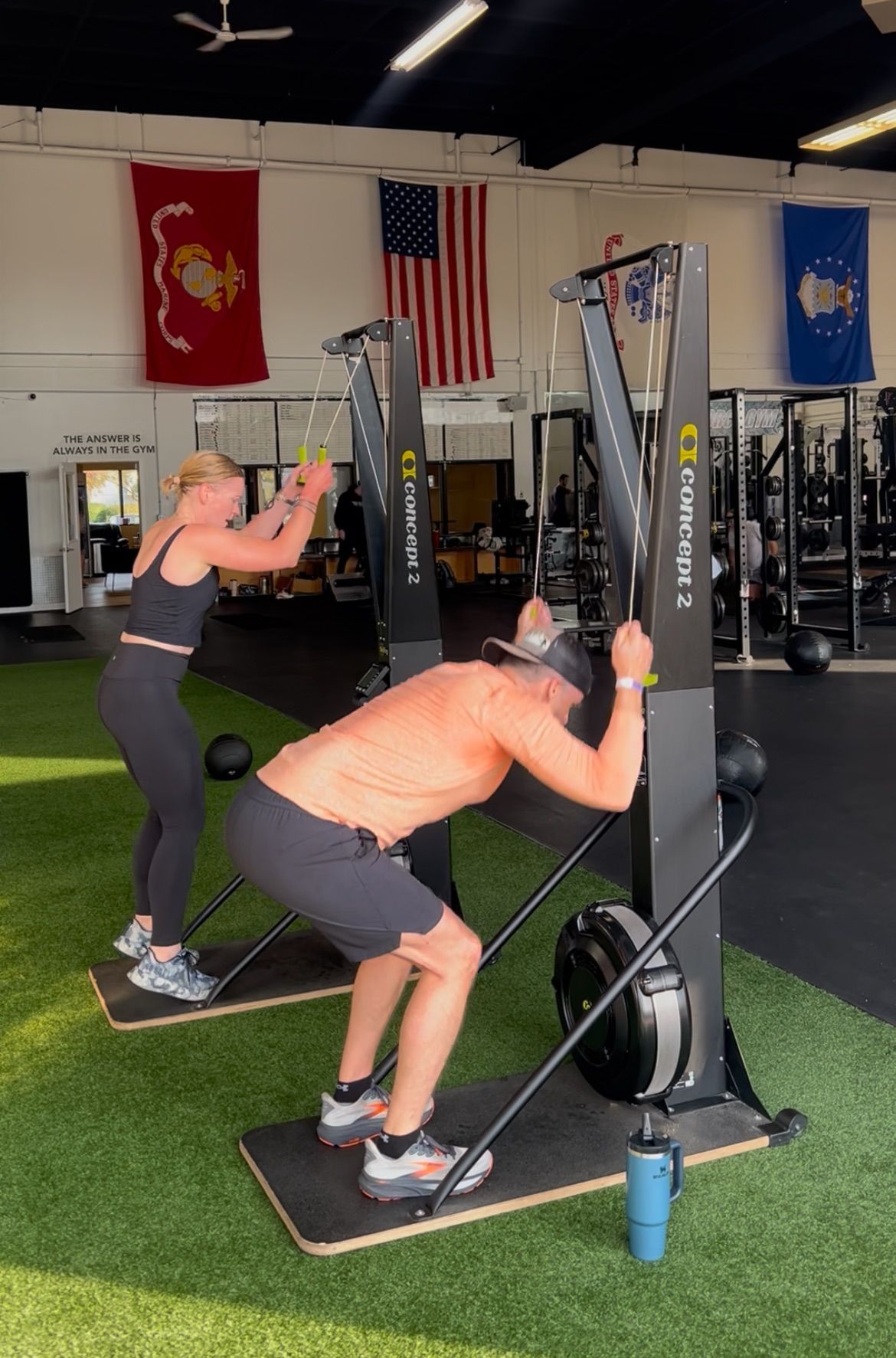 Woman doing kettlebell squat, guided by a trainer in a gym setting.