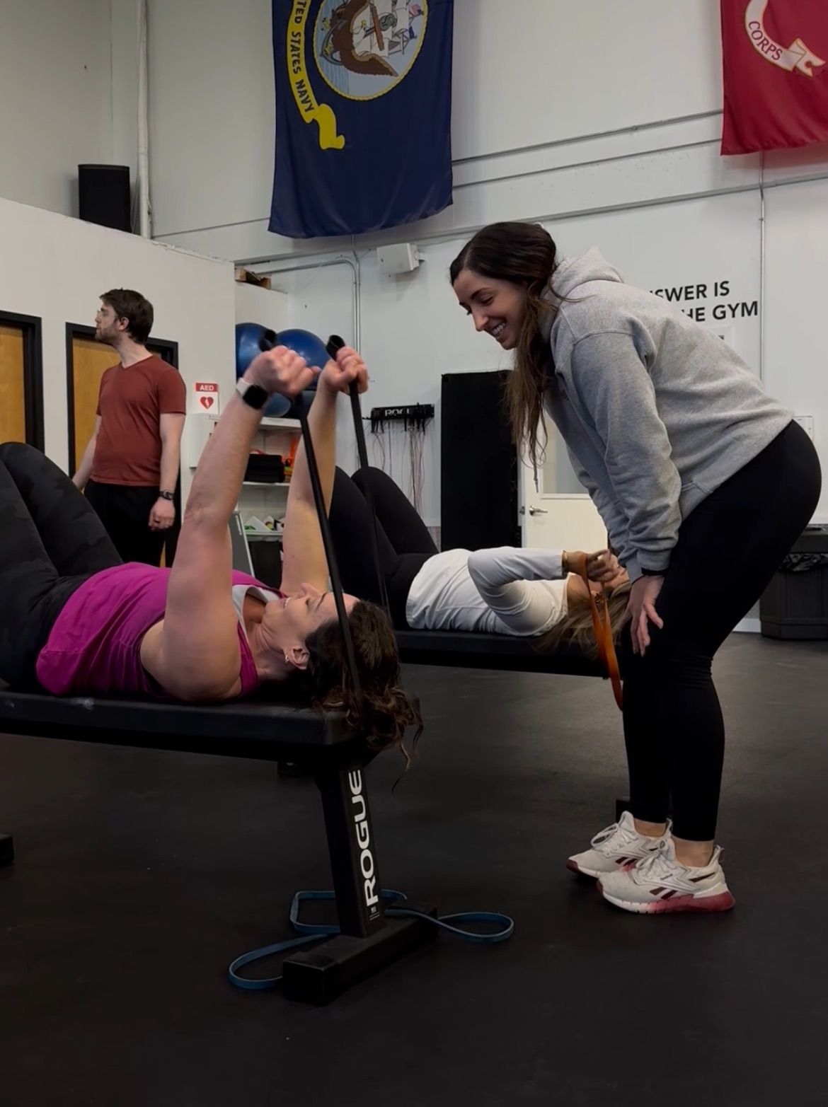 Trainer guides a man holding a kettlebell in a gym, adjusting his grip.