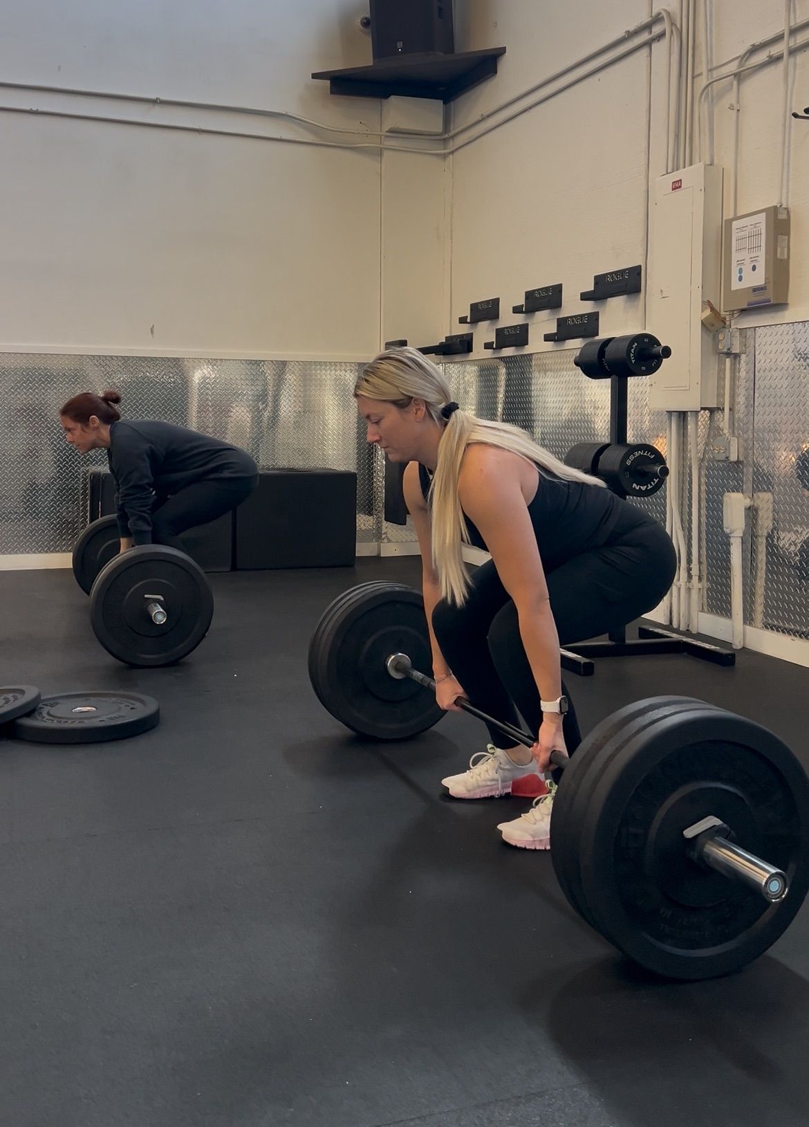 Man doing a squat with a barbell, supervised by a trainer in a gym.