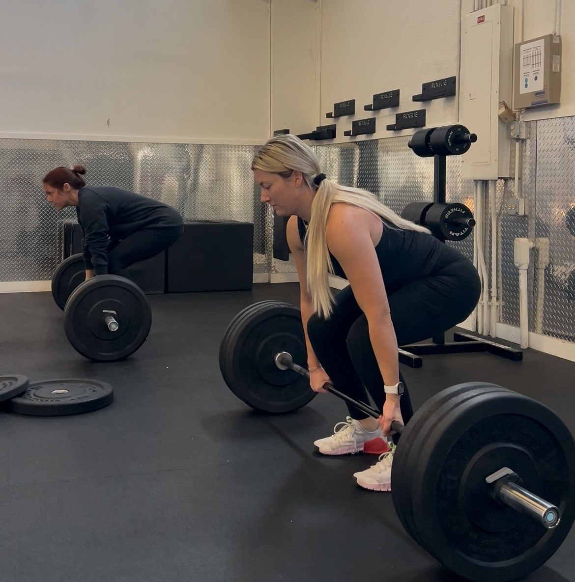 Man performing kettlebell squat exercise in gym, being supervised by trainer.