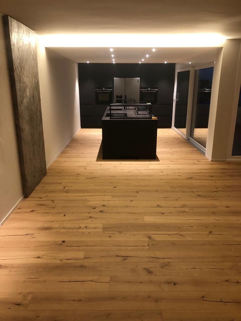 Holzboden in einer modernen Küche mit schwarzer Kochinsel und dunklen Schränken im Hintergrund.