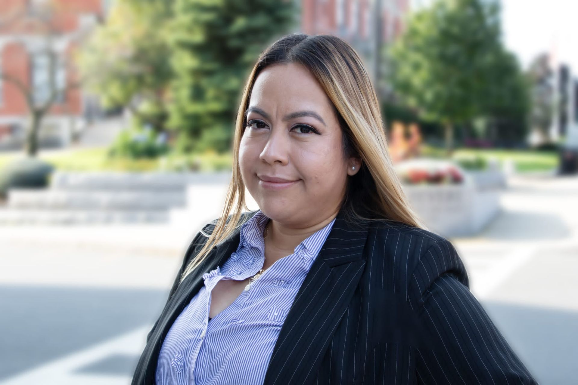 A woman in a suit and striped shirt is standing in front of a building.