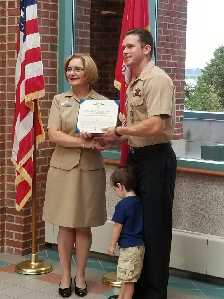 A man and a woman holding a certificate in front of an american flag