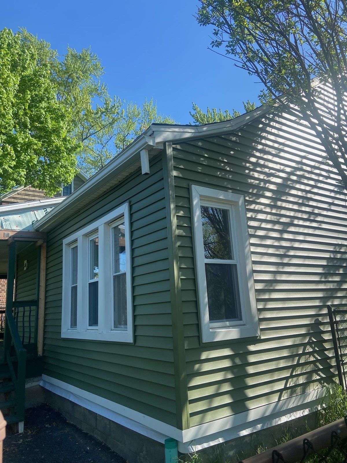 A green house with white trim and windows on a sunny day.  - Kingston, NY - JMD Home Improvements