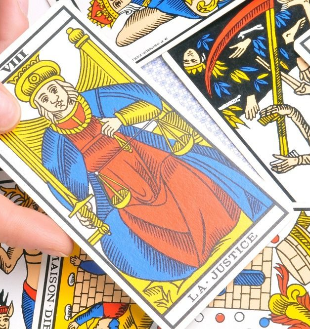 Carta del Tarot, La Justicia: figura con espada y balanza, en rojo, azul y amarillo; sosteniendo la carta.