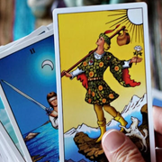 Persona sosteniendo cartas del tarot, con la carta del Loco en primer plano