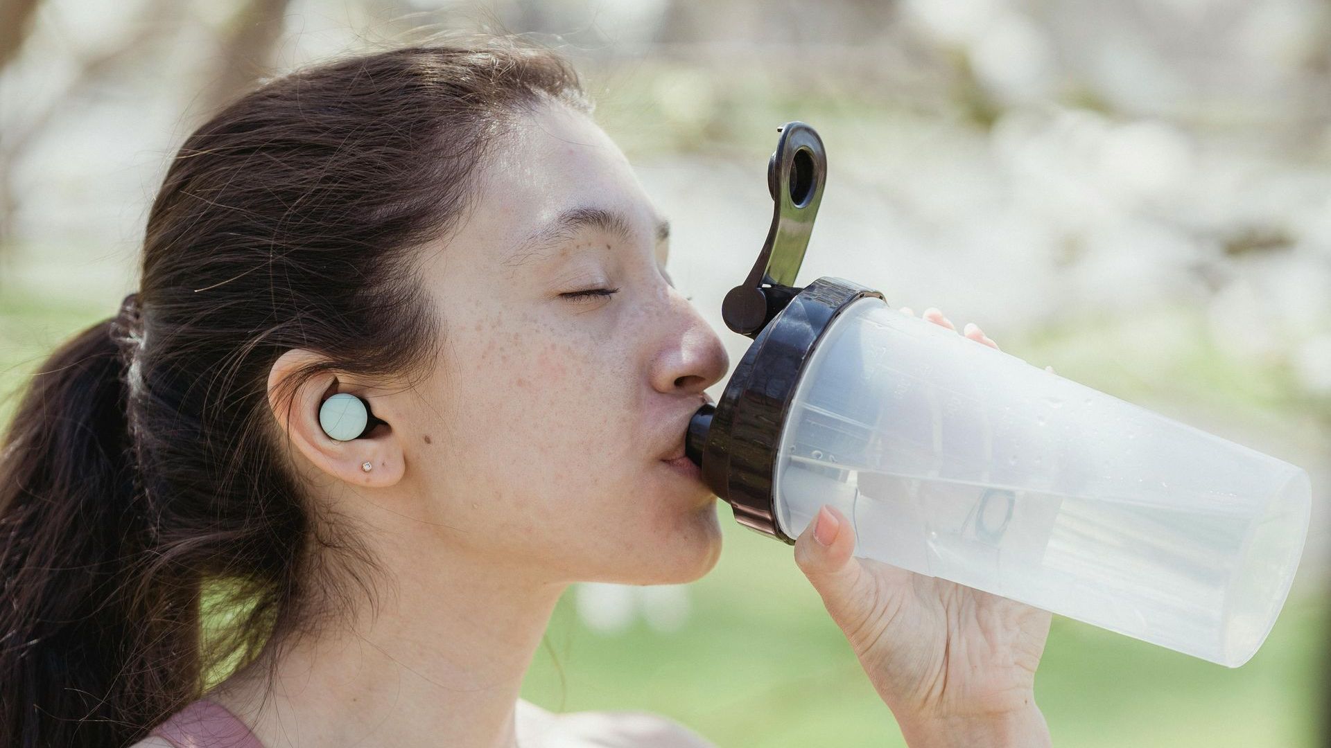Smiling woman drinking water outdoors on a sunny day