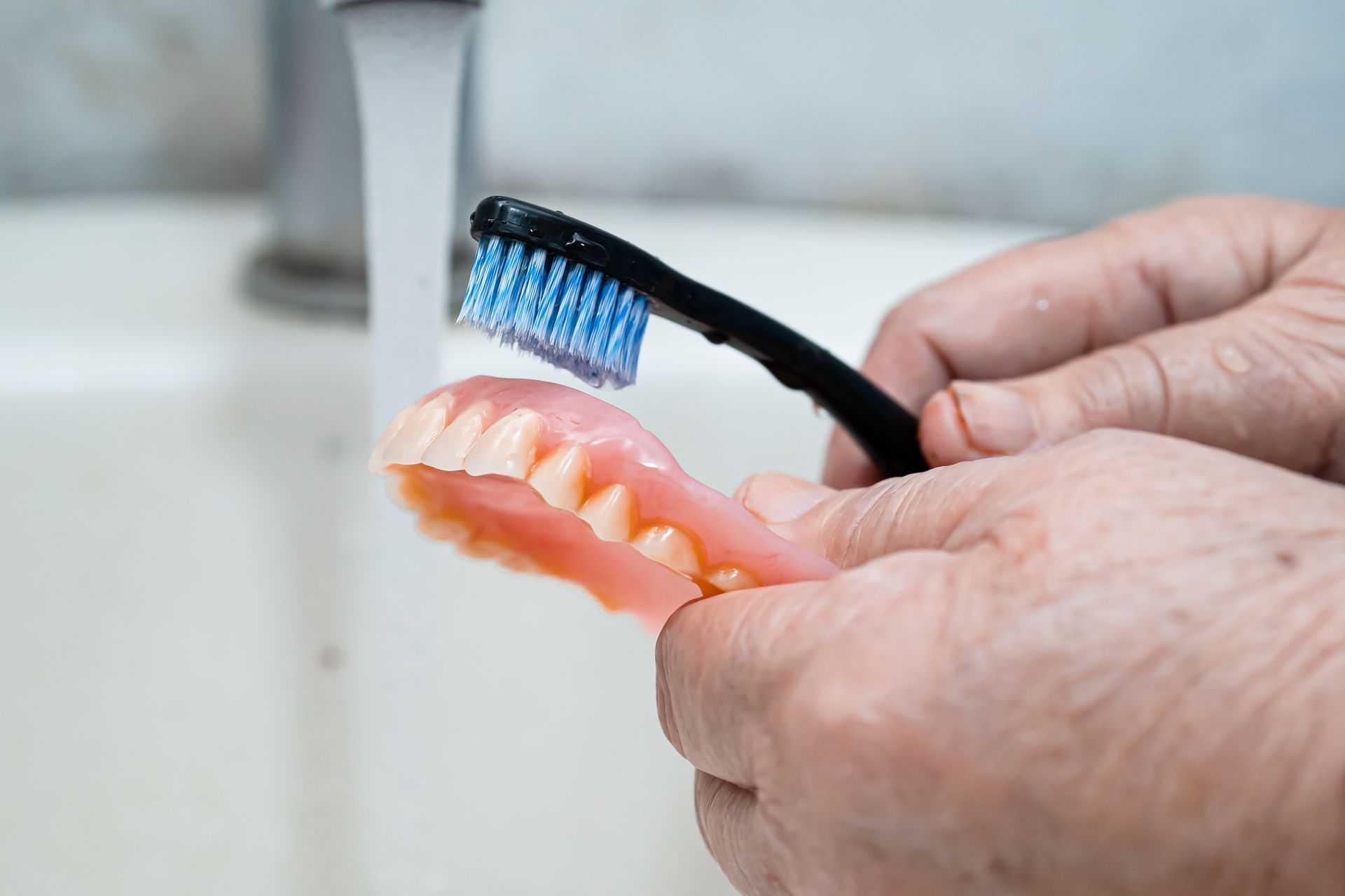 a woman carefully cleaning her dentures to maintain oral hygiene, highlighting the importance of dental care for seniors.
