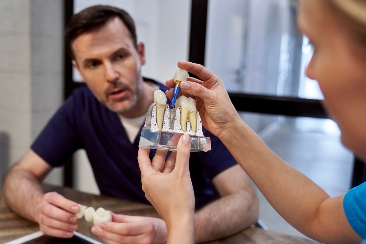 A dentist explains a dental implant model to a patient in an office setting.