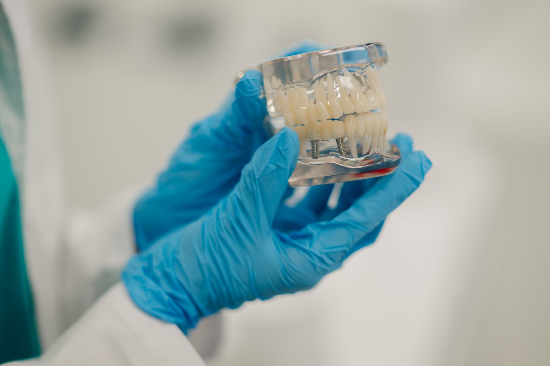 Blue-gloved hands hold a small clear glass container with pale beige material inside.
