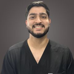 A man with a beard is wearing a black scrub top and smiling.