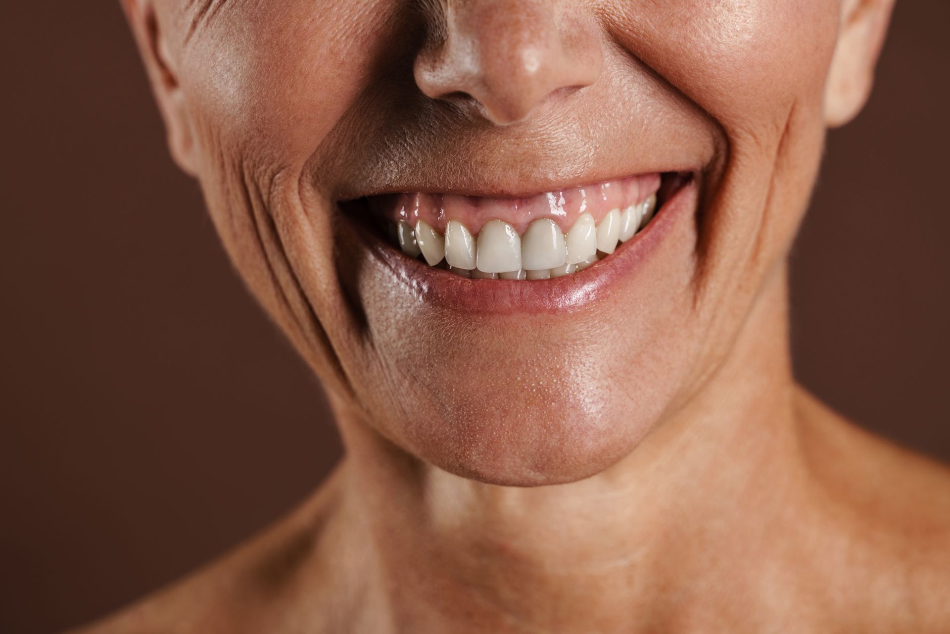 Smiling face with prominent wrinkles, showing teeth. Brown background.