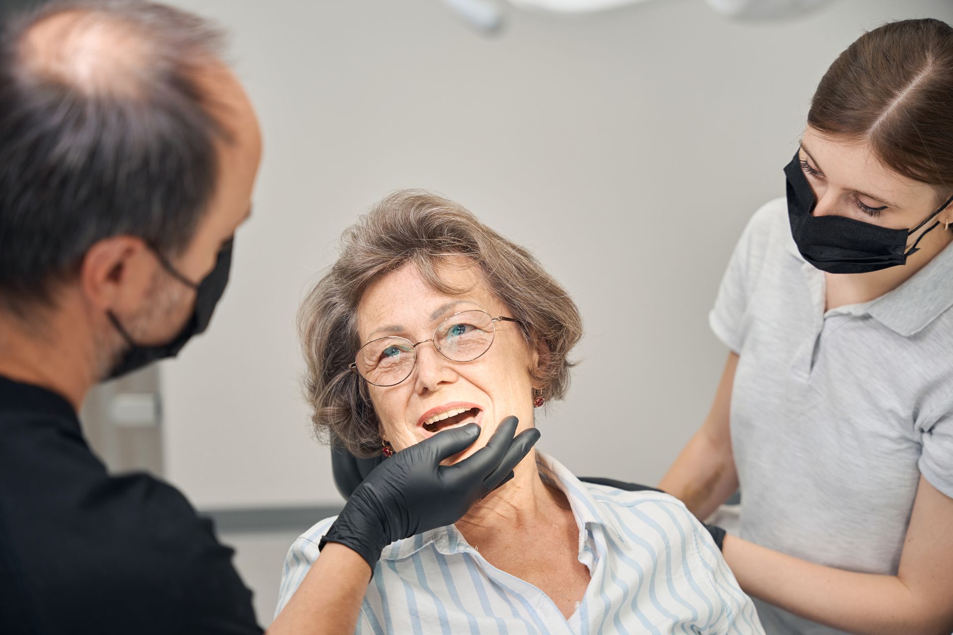 Dentist examining a patient’s mouth while an assistant stands nearby in a clinic